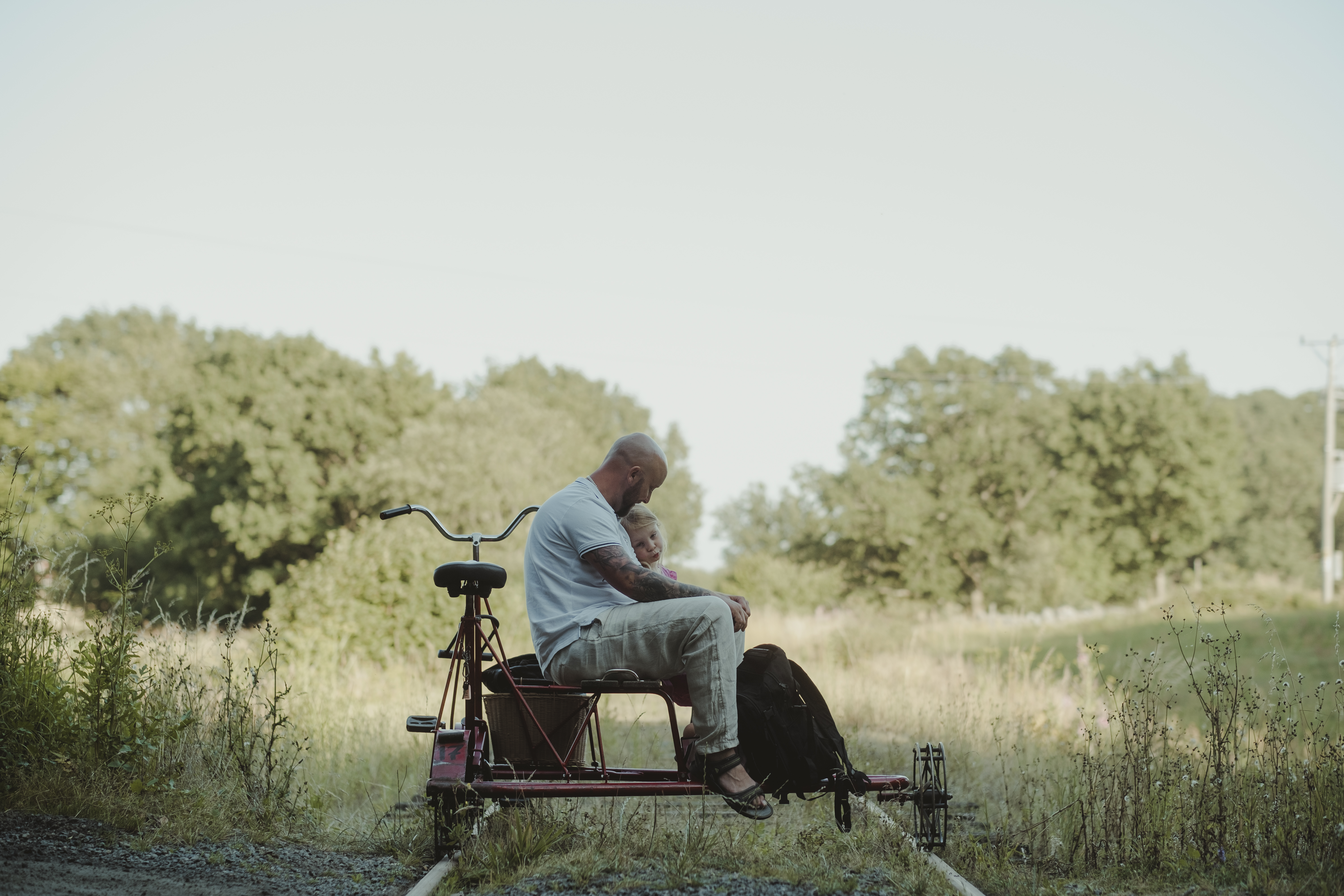 En far sitter tillsammans med sin dotter på en dressin cykel omgiven av naturen