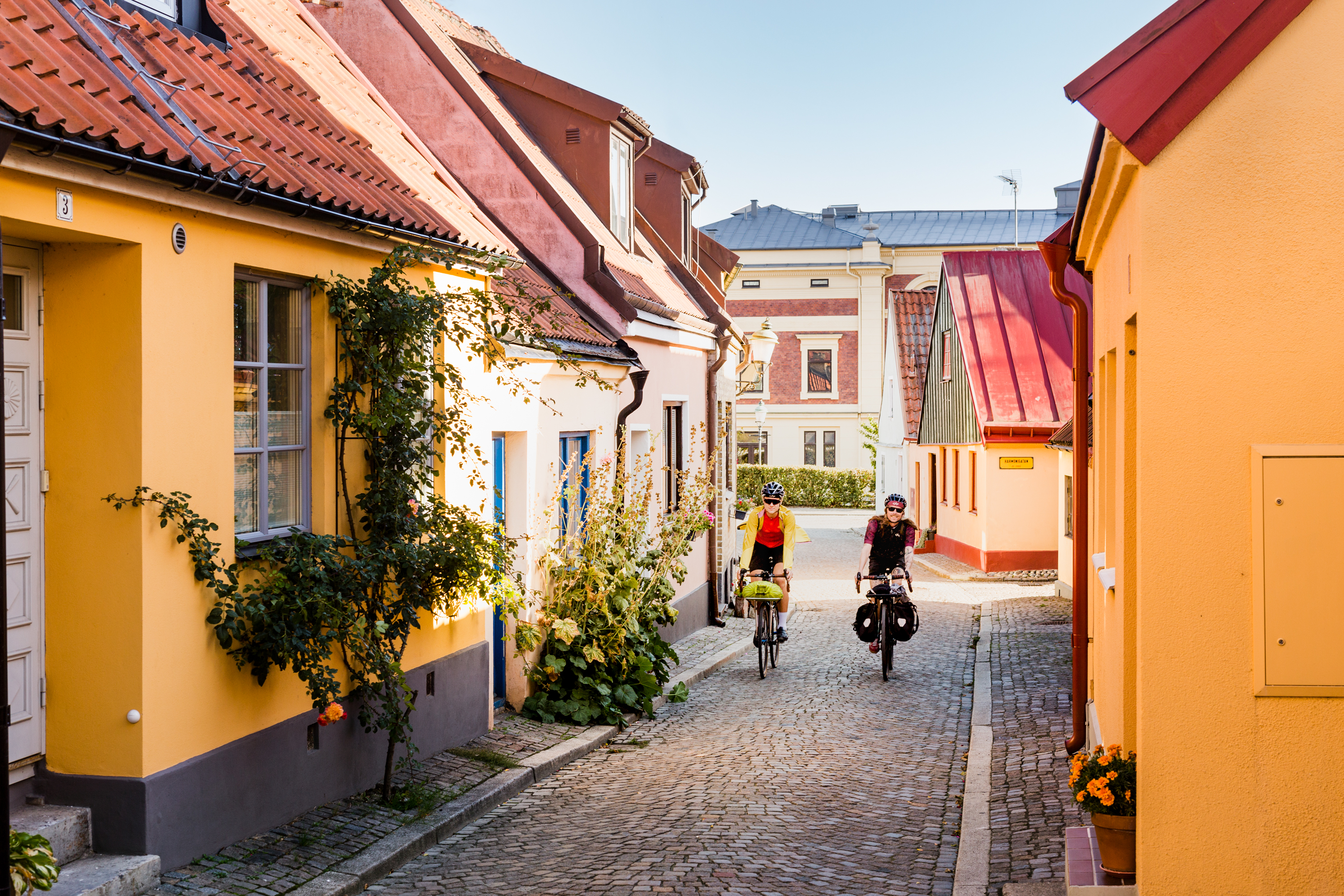 Two cyclists come cycling on a cobbled street among picturesque houses.