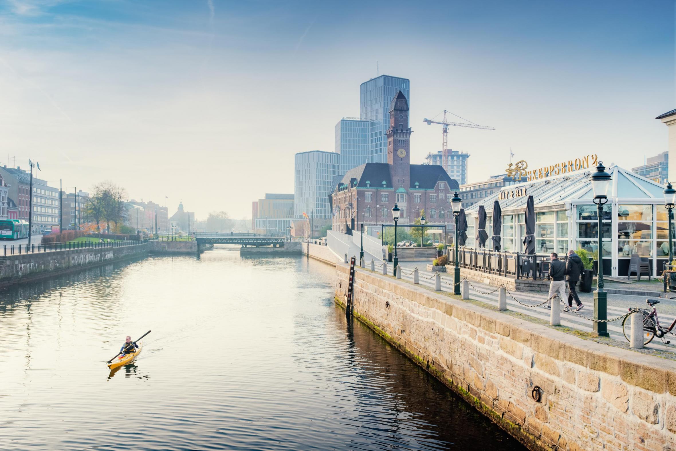 En person paddlar kayak i Malmö kanal, med Malmö Live i bakgrunden.