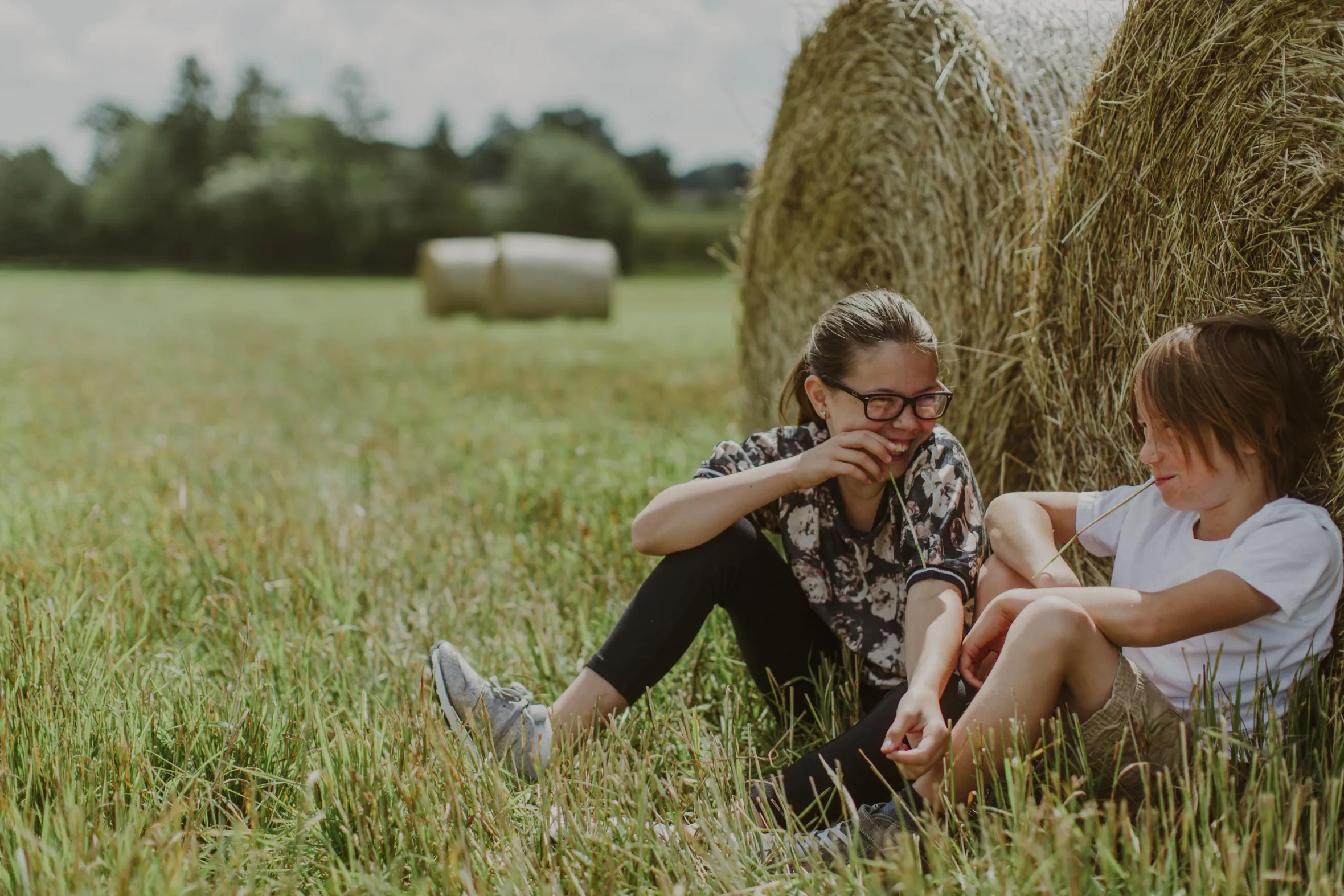 Two children sit next to hay bales in a field