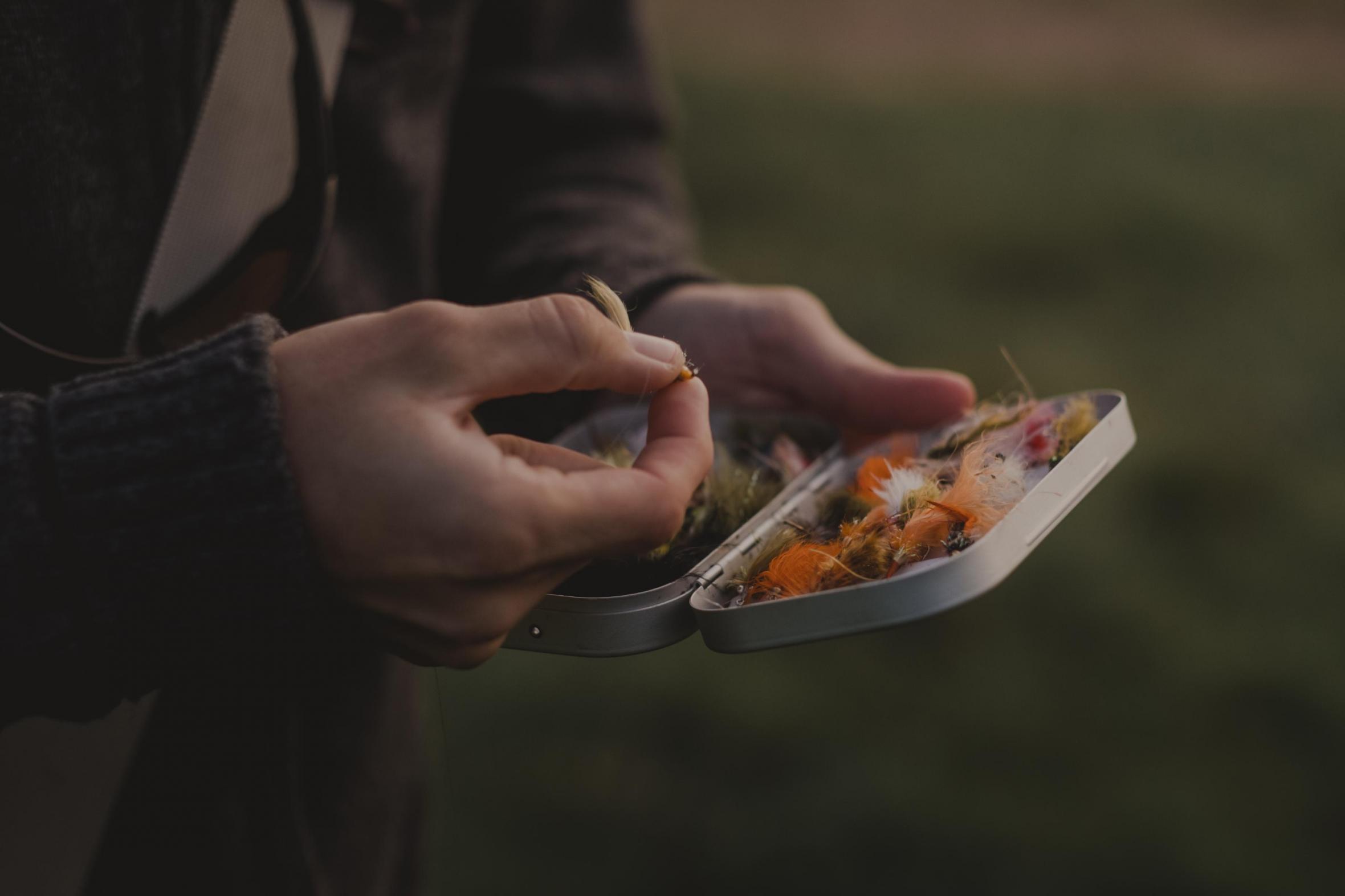 Nahaufnahme der Hände eines Mannes, die eine Metalldose mit Ködern zum Angeln halten