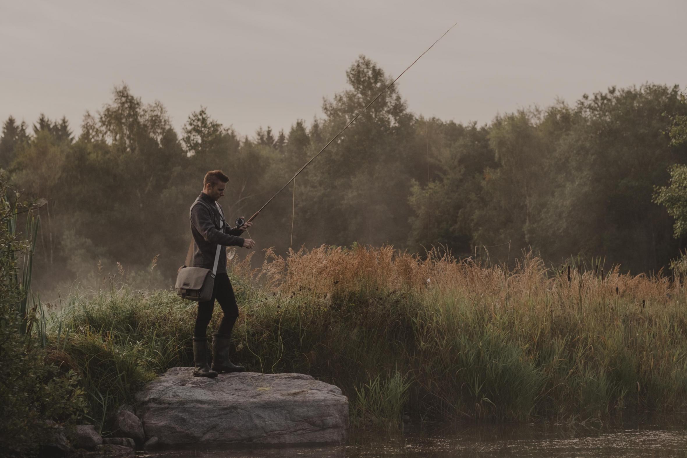 Ein Mann angelt an einem nebligen Morgen mit dem Wald im Hintergrund