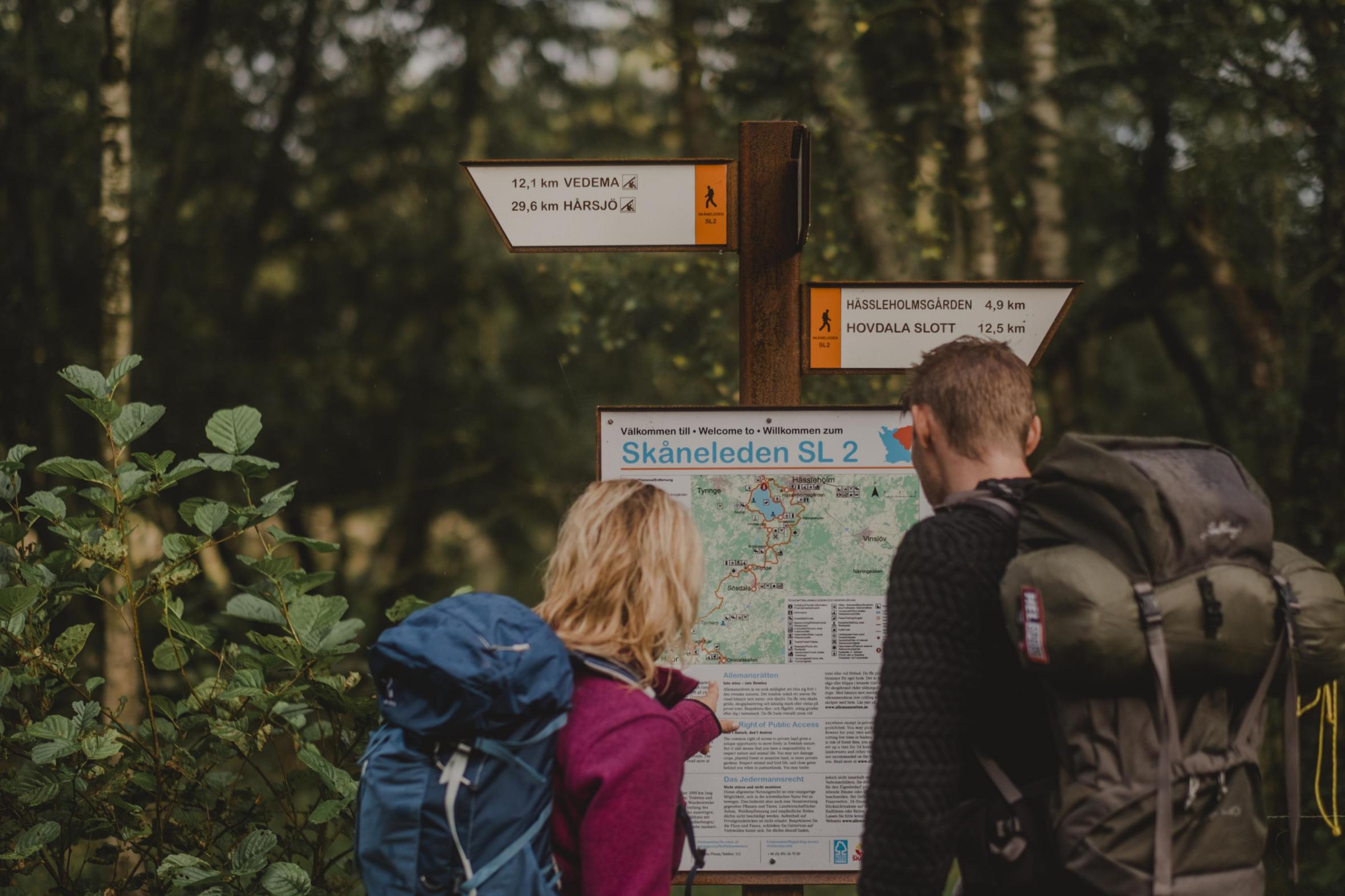 Ein Paar studiert ein Infoschild mit Karte am Wanderweg Skåneleden.