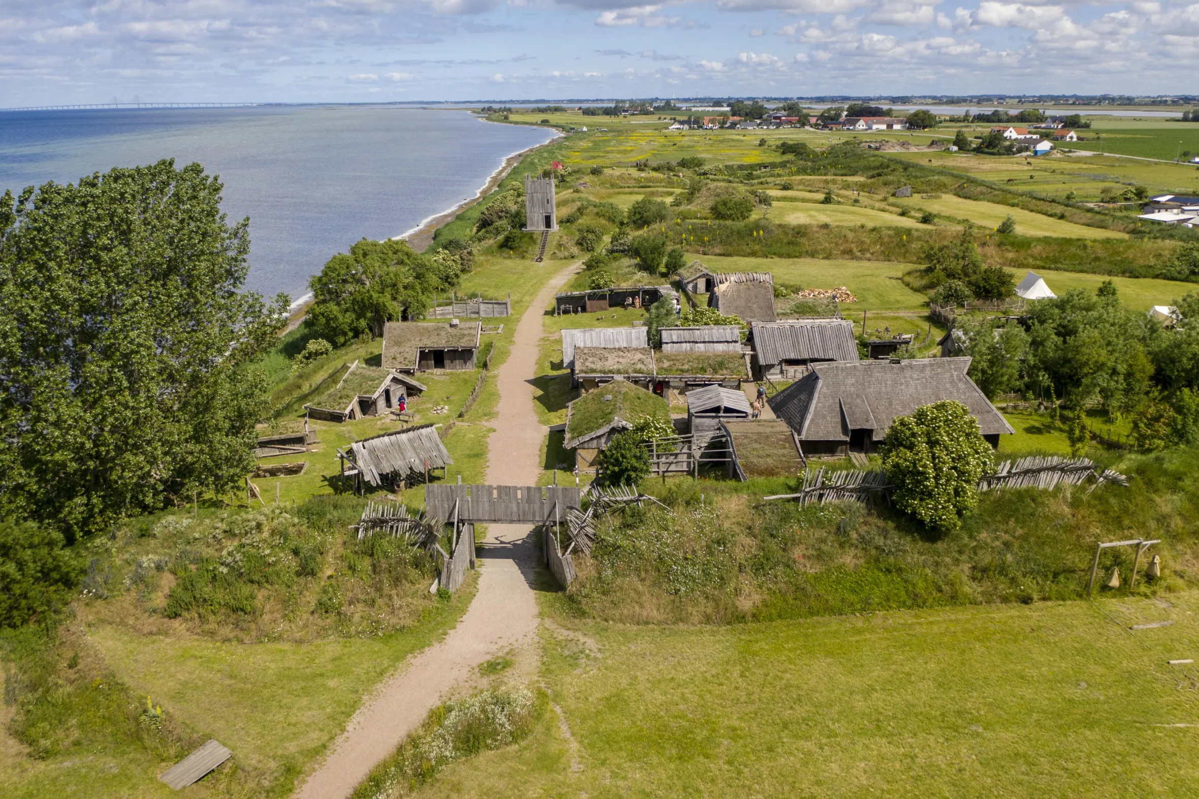 Fotevikens Museum och vikingaby ovanifrån, omgiven av gröna fält och havet i bakgrunden
