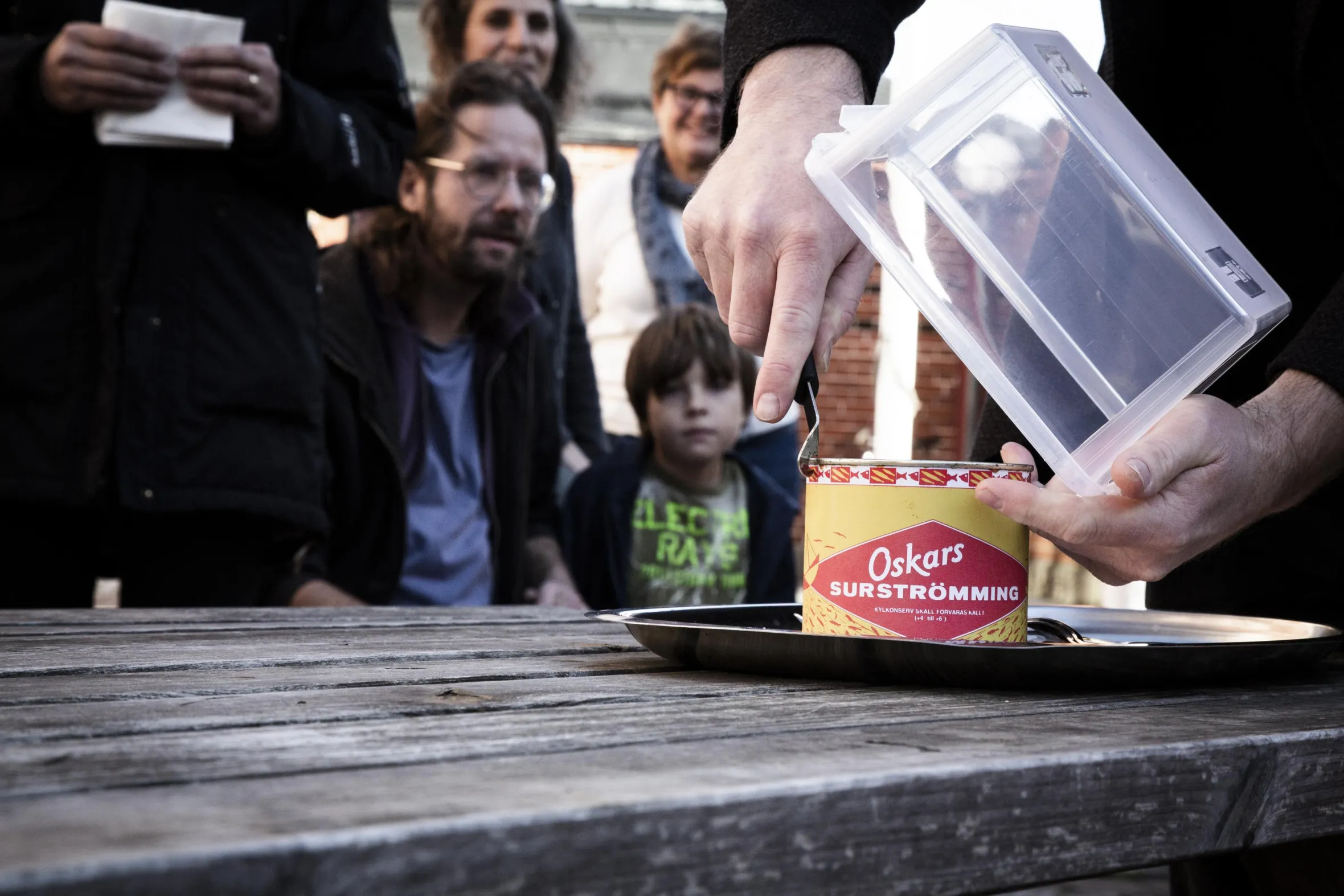 Mehrere Leute sehen zu, wie jemand im Freien eine Dose vergorenen Hering (Surströmming) öffnet.