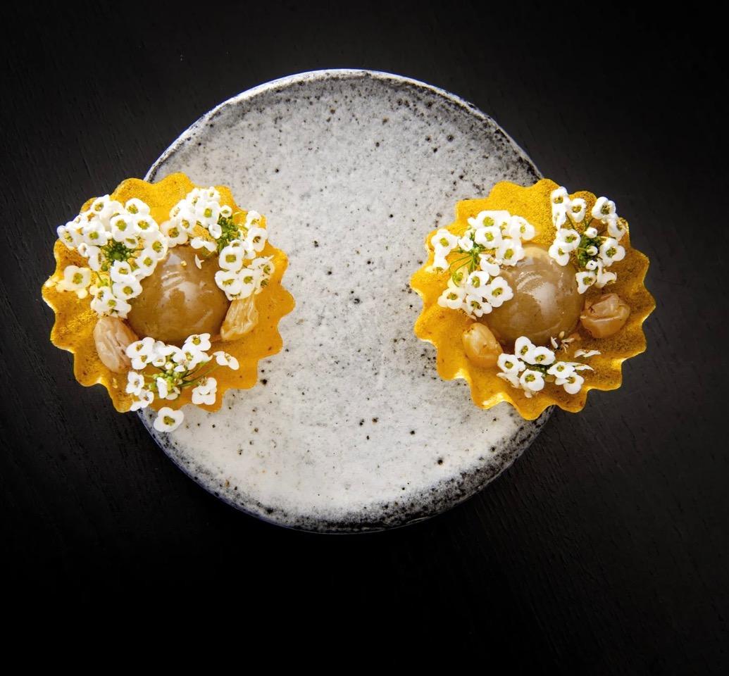 Two delicate tartlets adorned with tiny white edible flowers, artfully presented on a ceramic plate