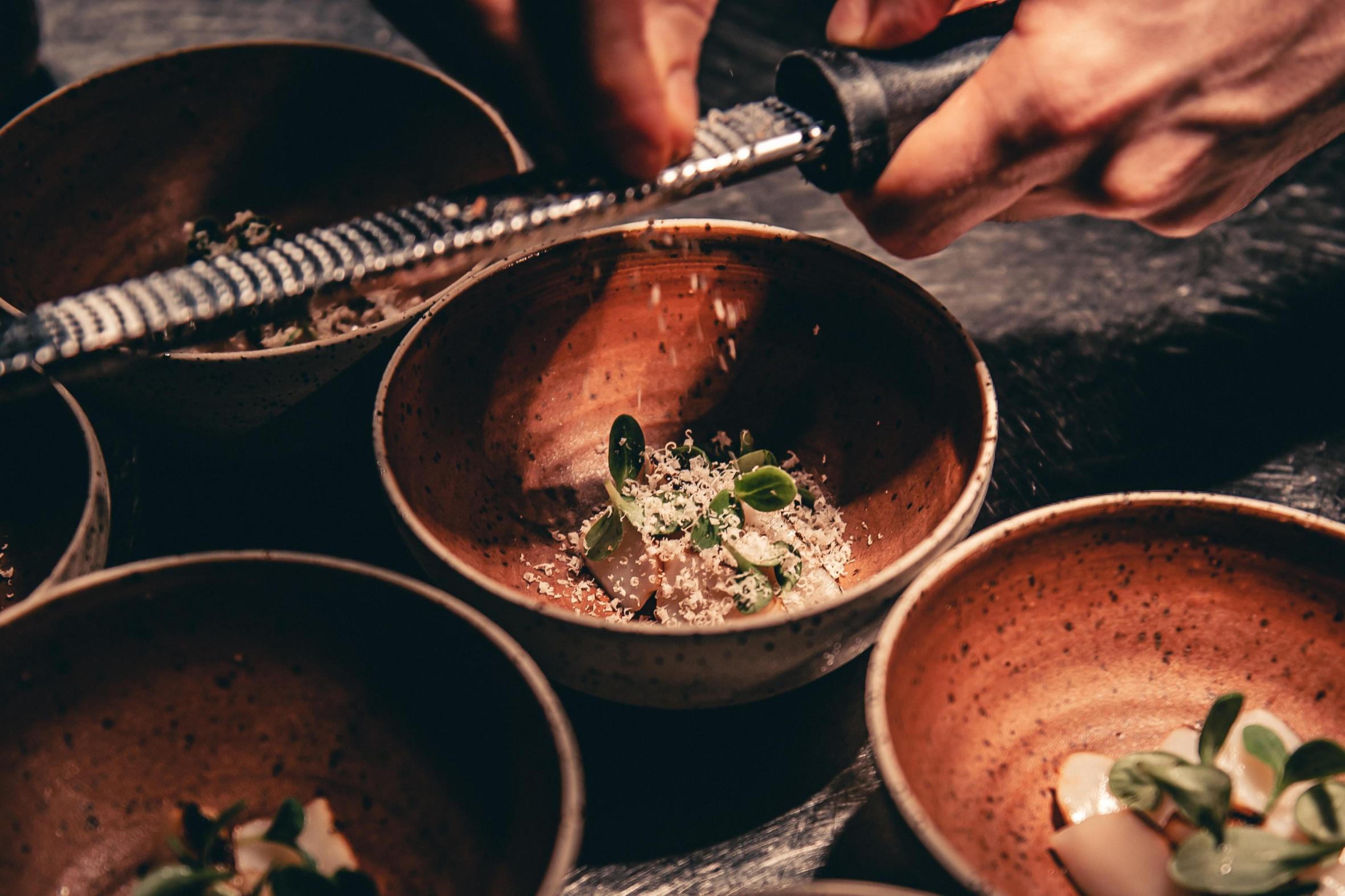Chef grating something over a small gourmet dish in ceramic bowls