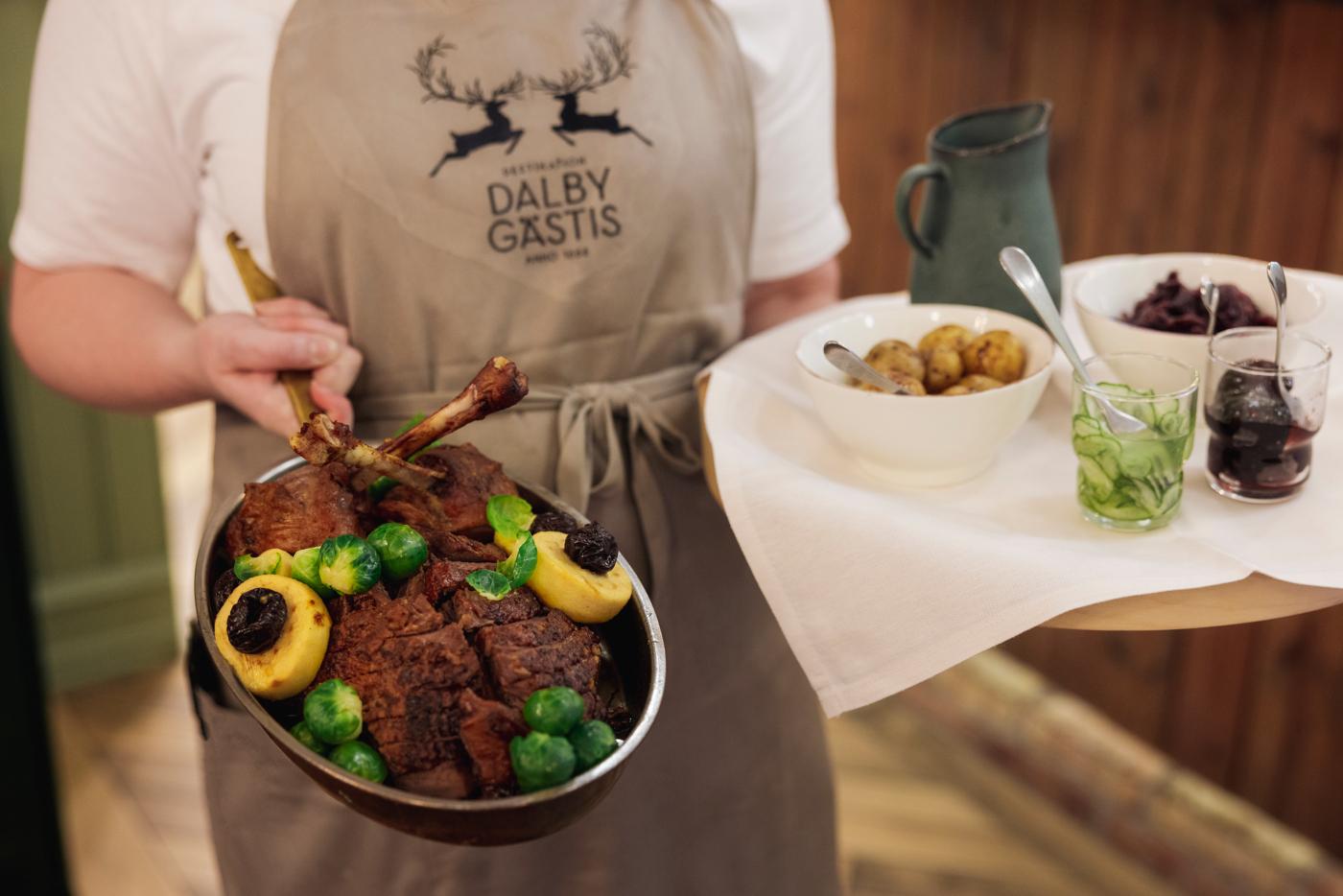 Chef holding a tray and a pan with oven-baked goose and its sides