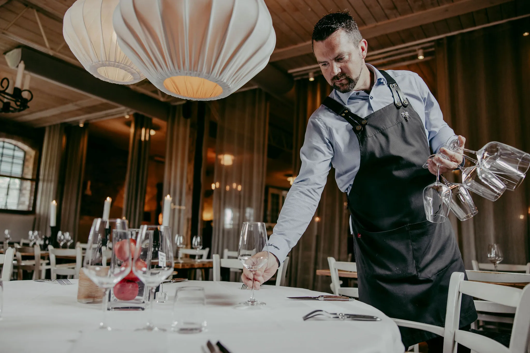 Male waiter sets a table with wine glasses in a chic restaurant interior