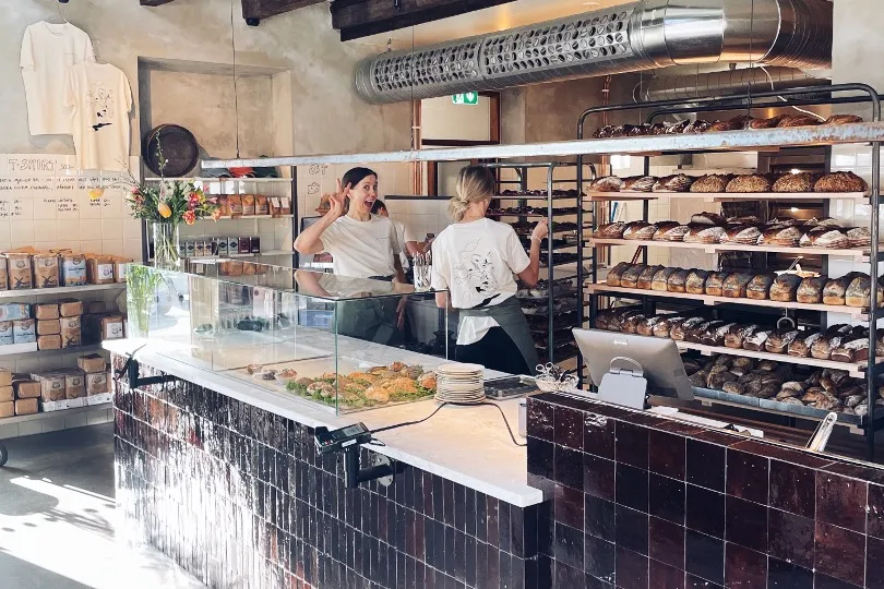Two happy women standing behind a bakery counter with freshly baked bread beside them