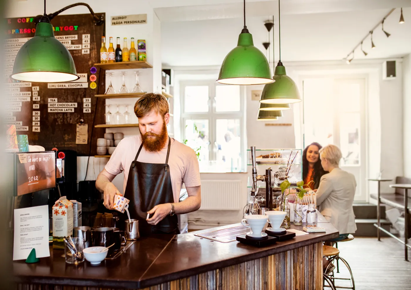 Male barista preparing coffee behind a bar with green ceiling lamps