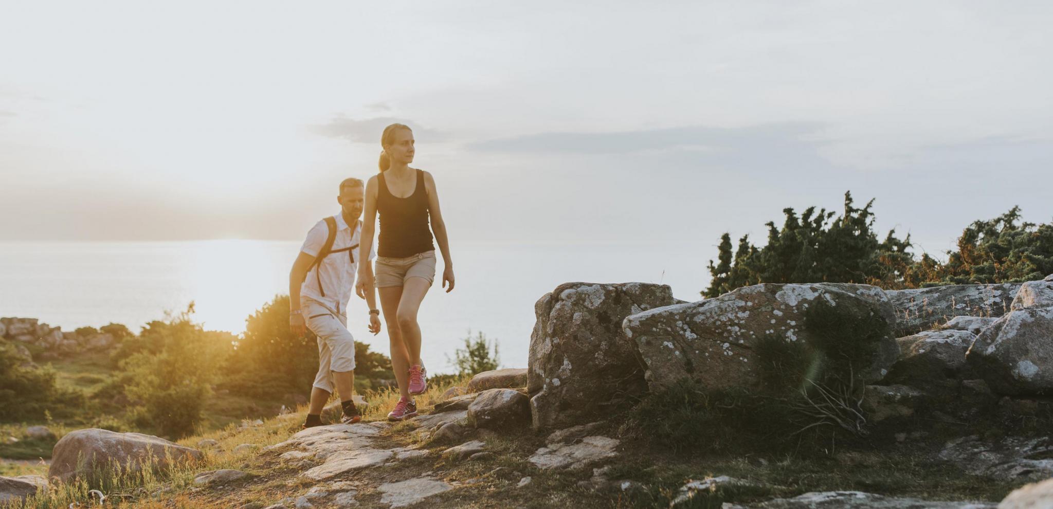 Ein junges Paar wandert bei Sonnenuntergang durch das Küstengebiet Hovs Hallar und hat das Meer im Hintergrund.