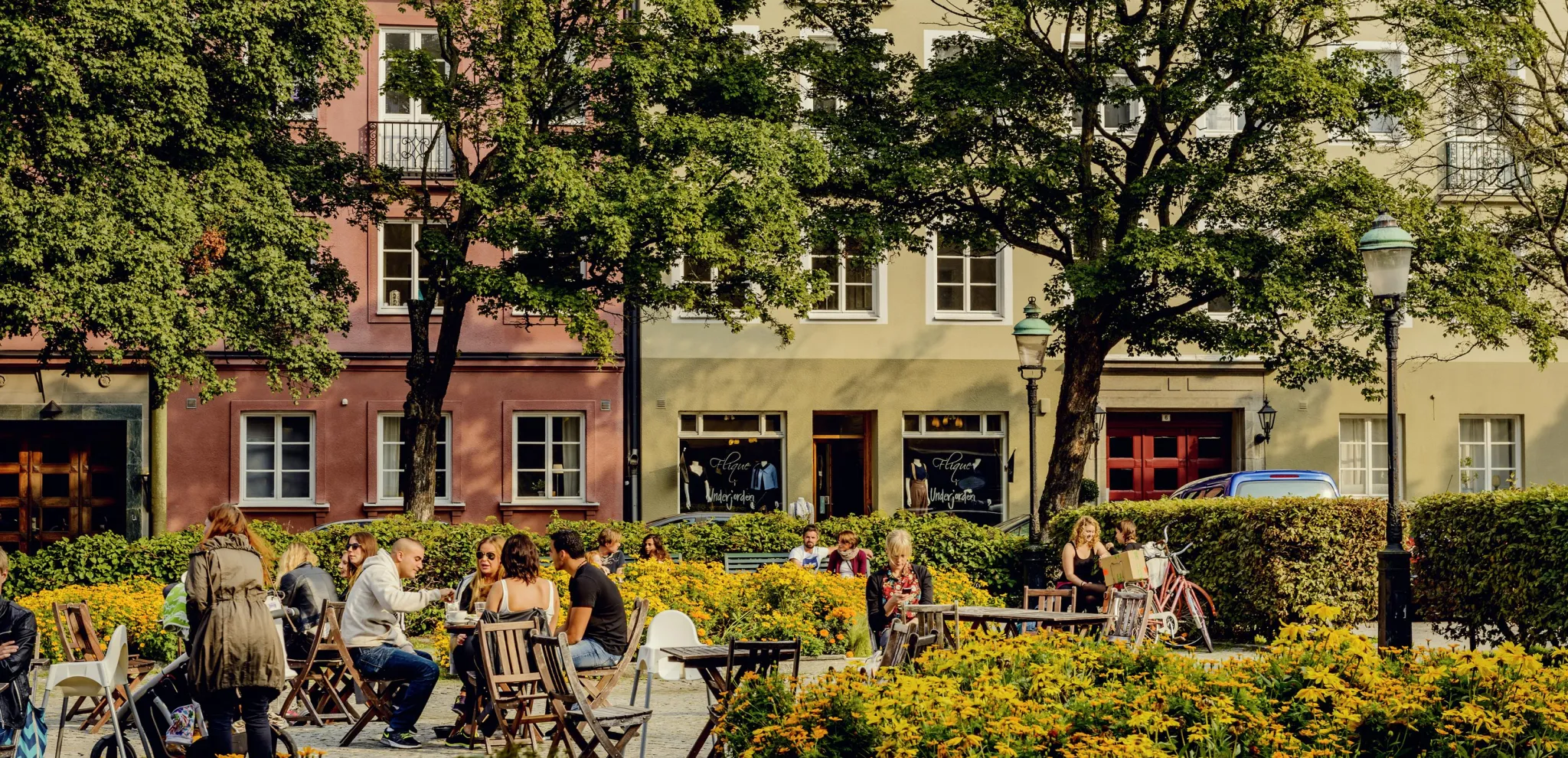 An einem Sommertag sitzen Leute im Freien auf dem begrünten Platz Davidshallstorget in Malmö.