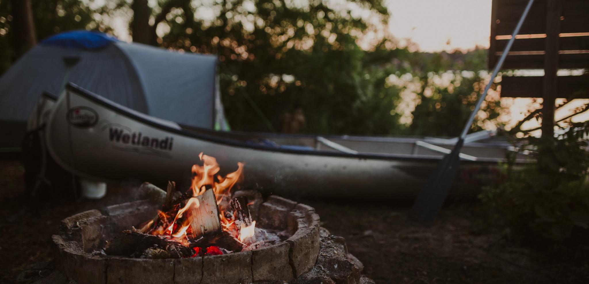 En lägerplats med en lägereld intill en kanot vid sjön Ivösjön
