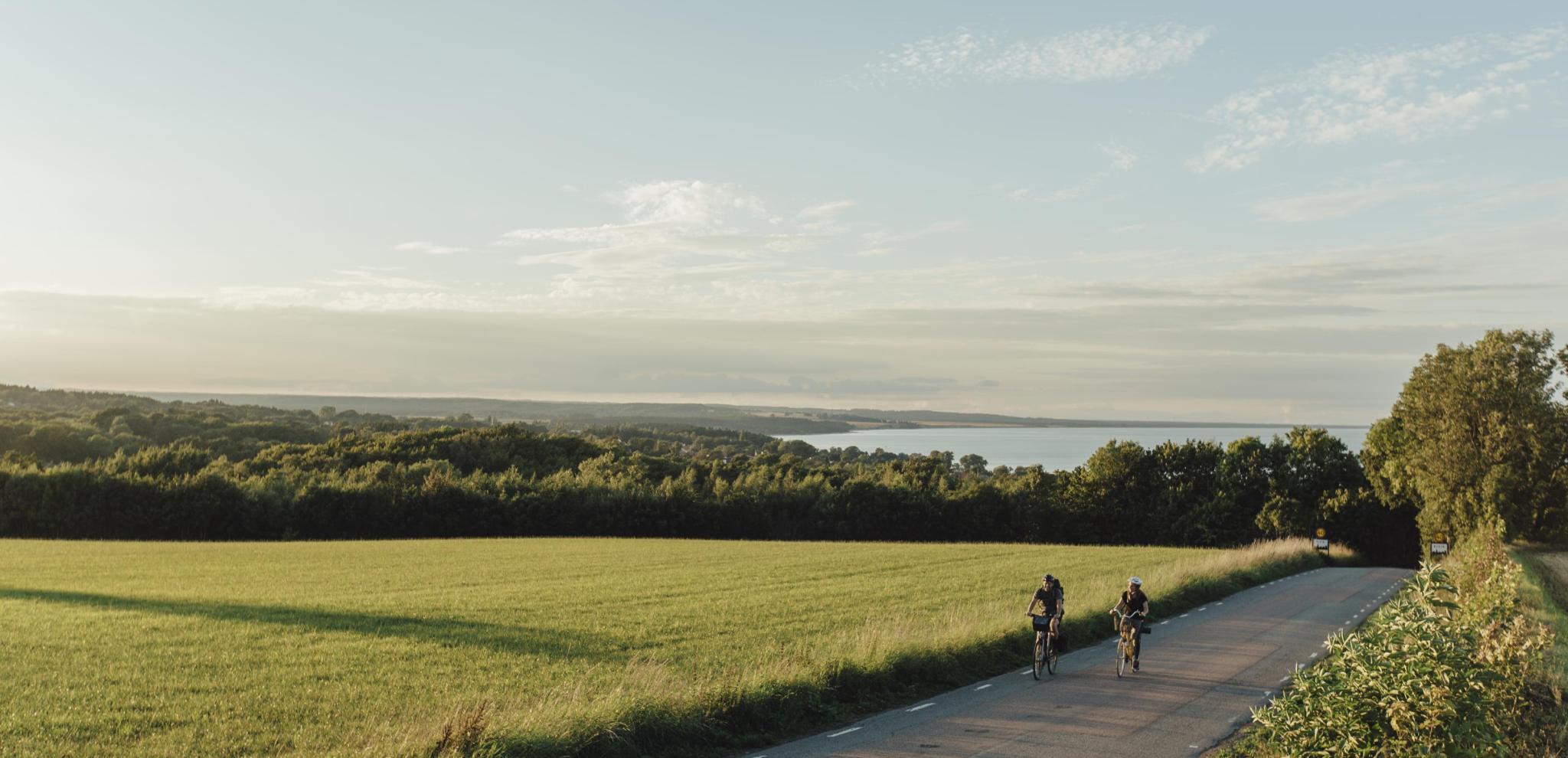 A couple cycling on a country road in Österlen, with a field and the sea in the background