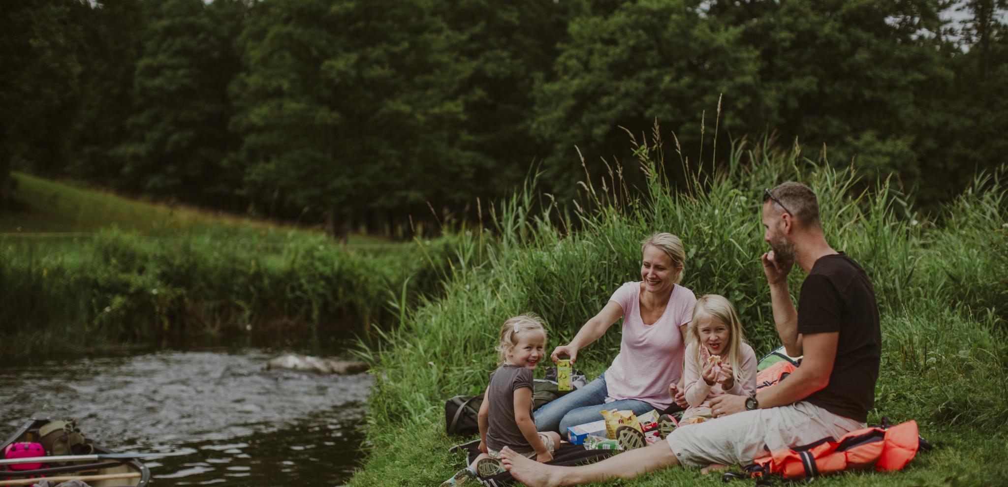 En Familjen sitter och njuter av en picknick vid flodstranden vid Rönne å
