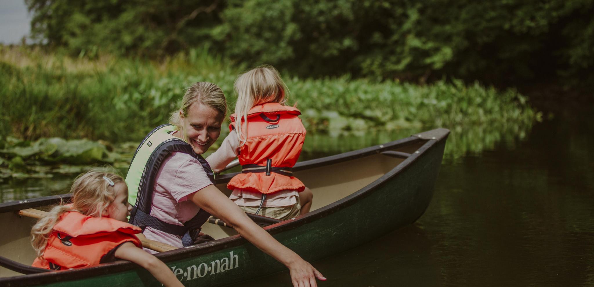 Barn och vuxen känner på vattnet i Rönne å.