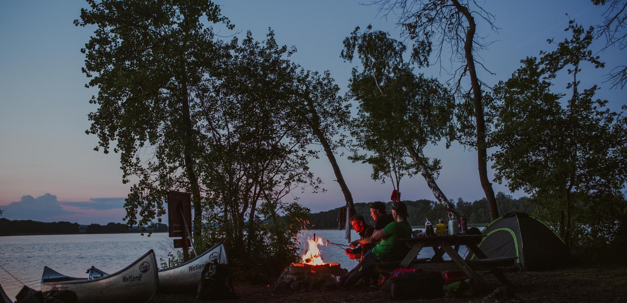 En grupp vänner grillar i skymningen intill Ivösjön