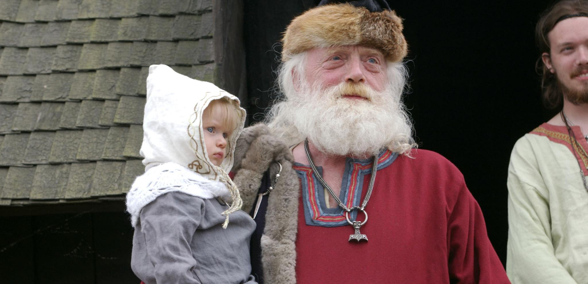 Ein verkleideter Wikinger mit weißem Bart hält ein kleines Kind im Arm.
