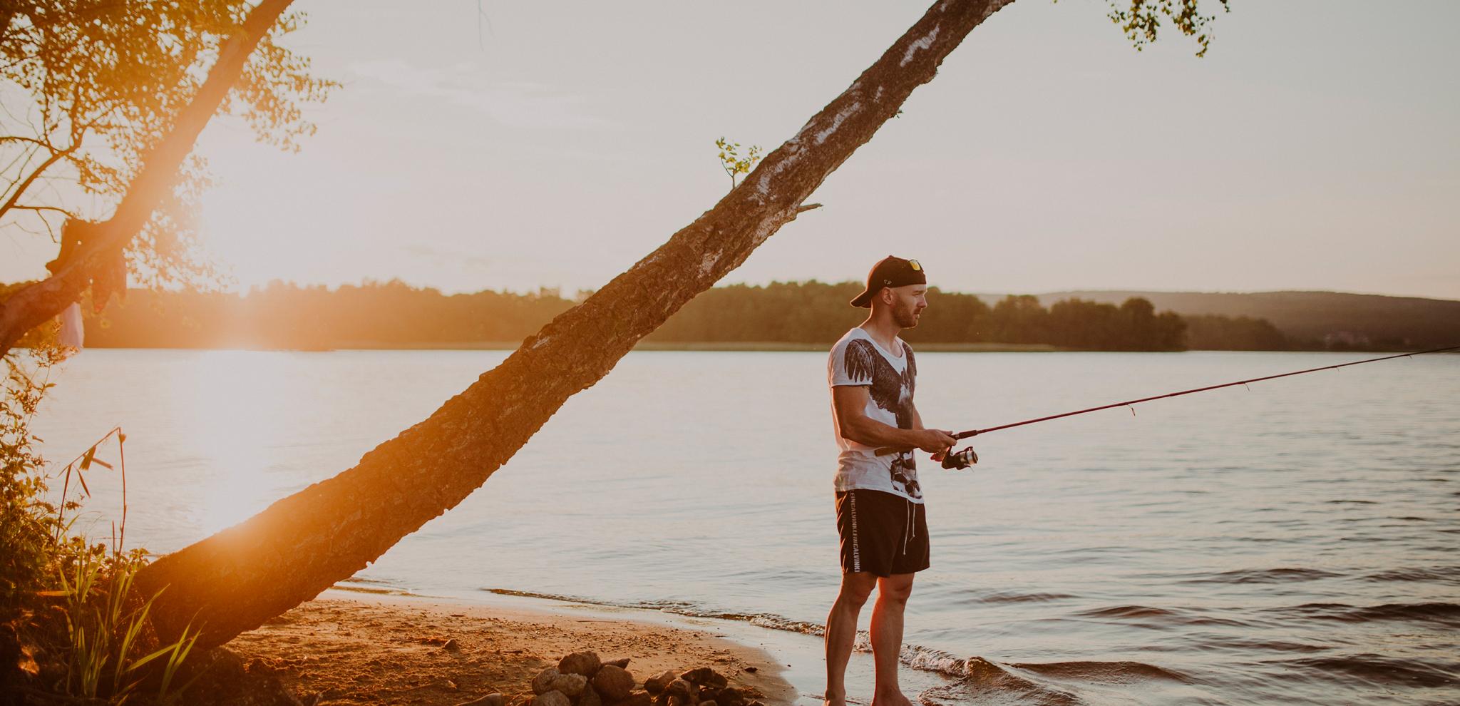 A man standing on the beach at lake Ivösjön fishing at sunset