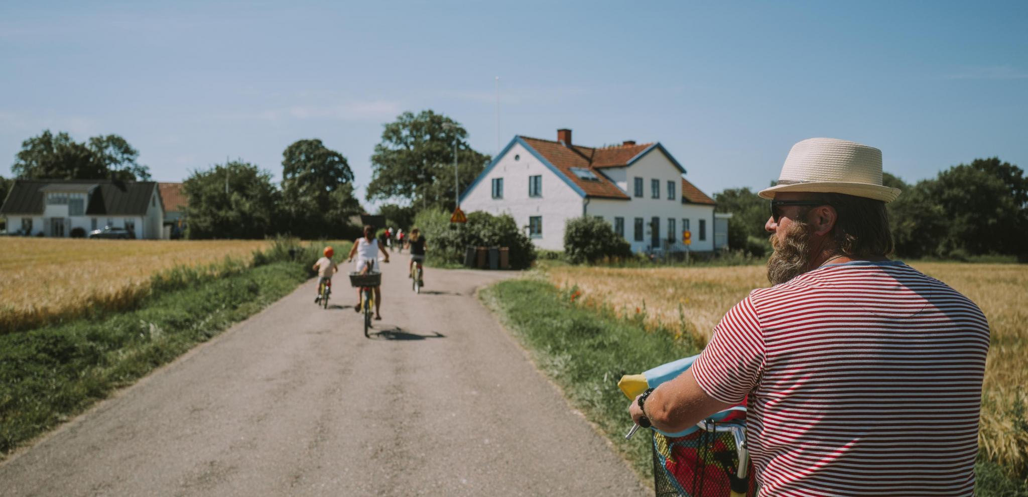 Family biking through the fields on a gravel road towards a white house on the island of Ven