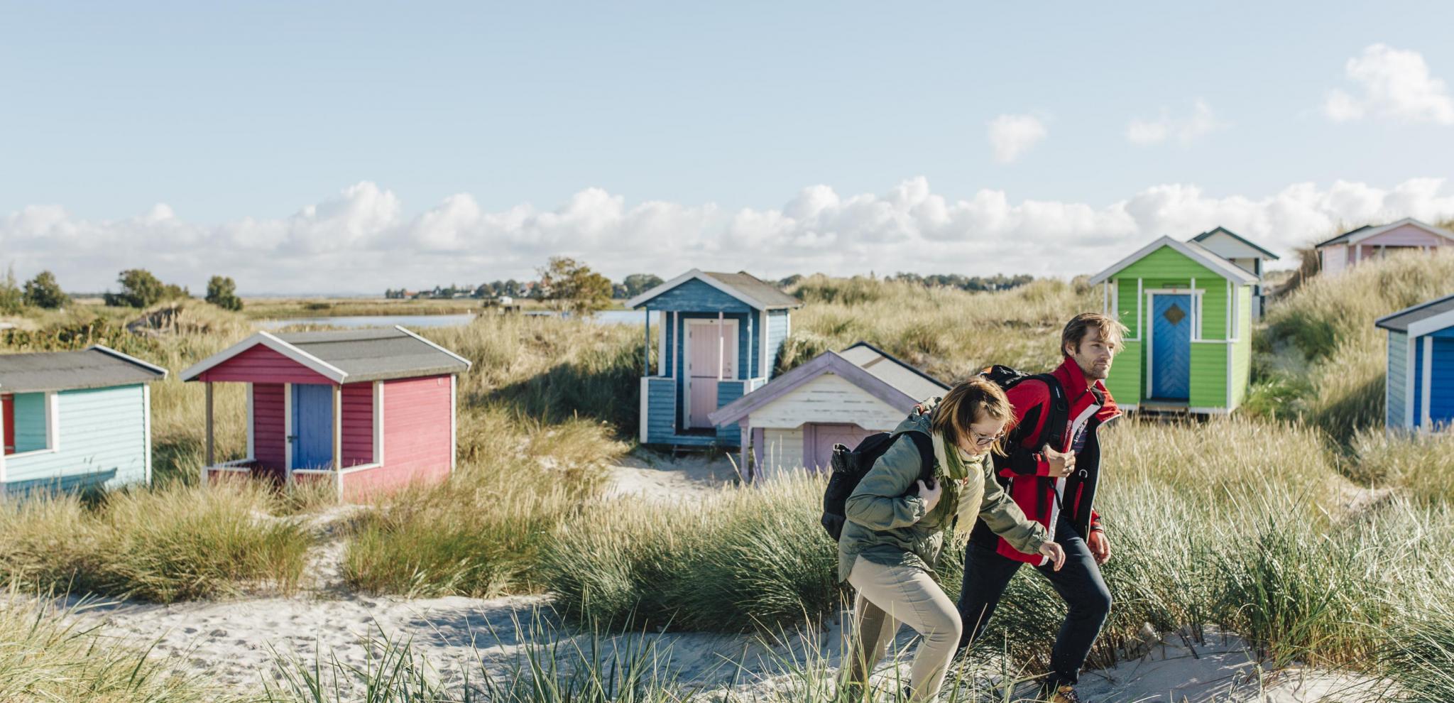 Couple hiking on sandunes with beach cabins