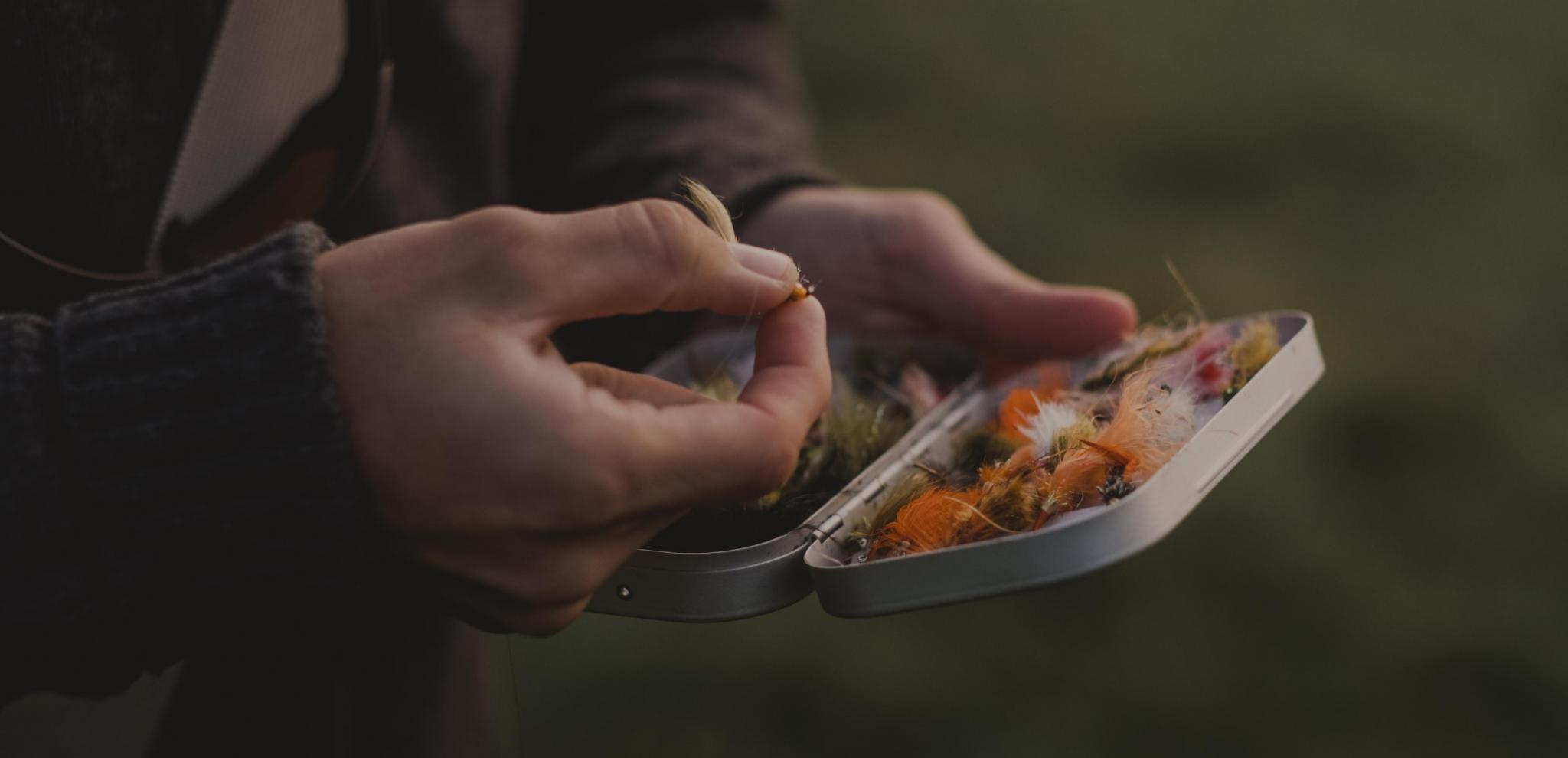 Hands holding a small metal case with fishing baits