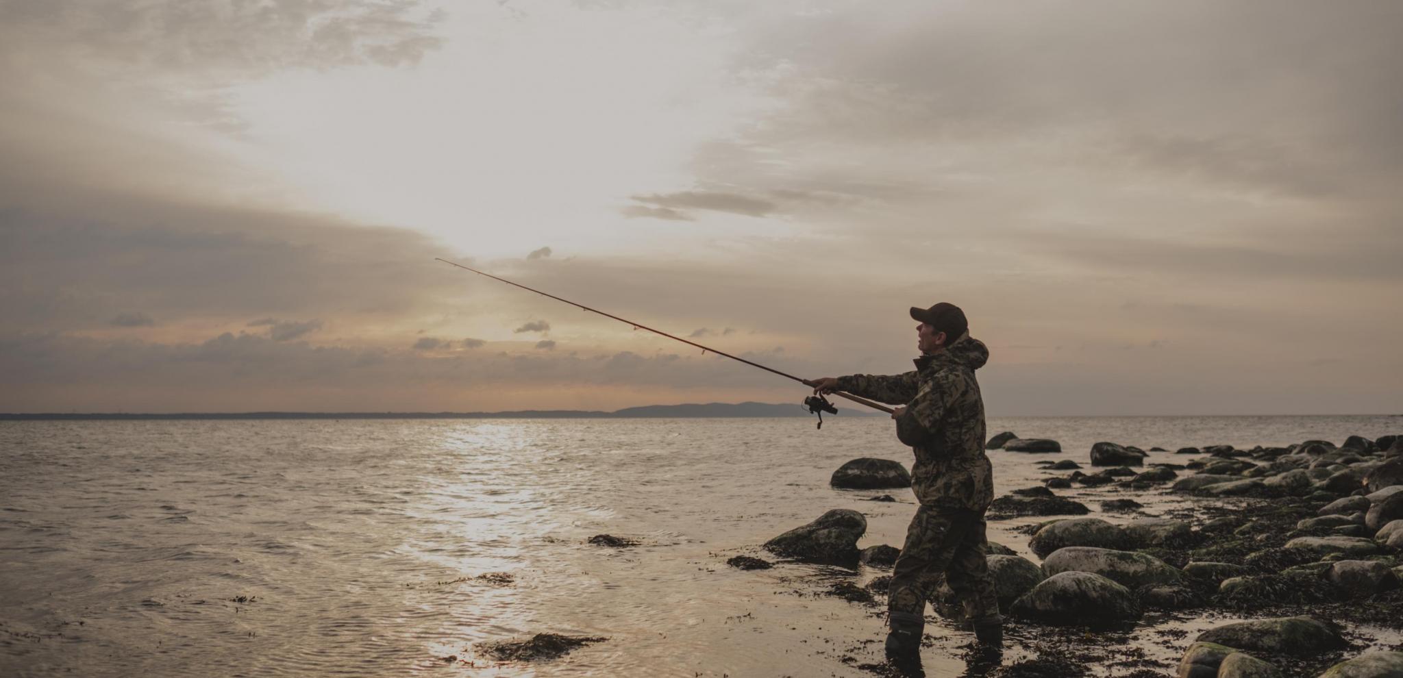 A fisherman throws with his fishing rod at sunrise