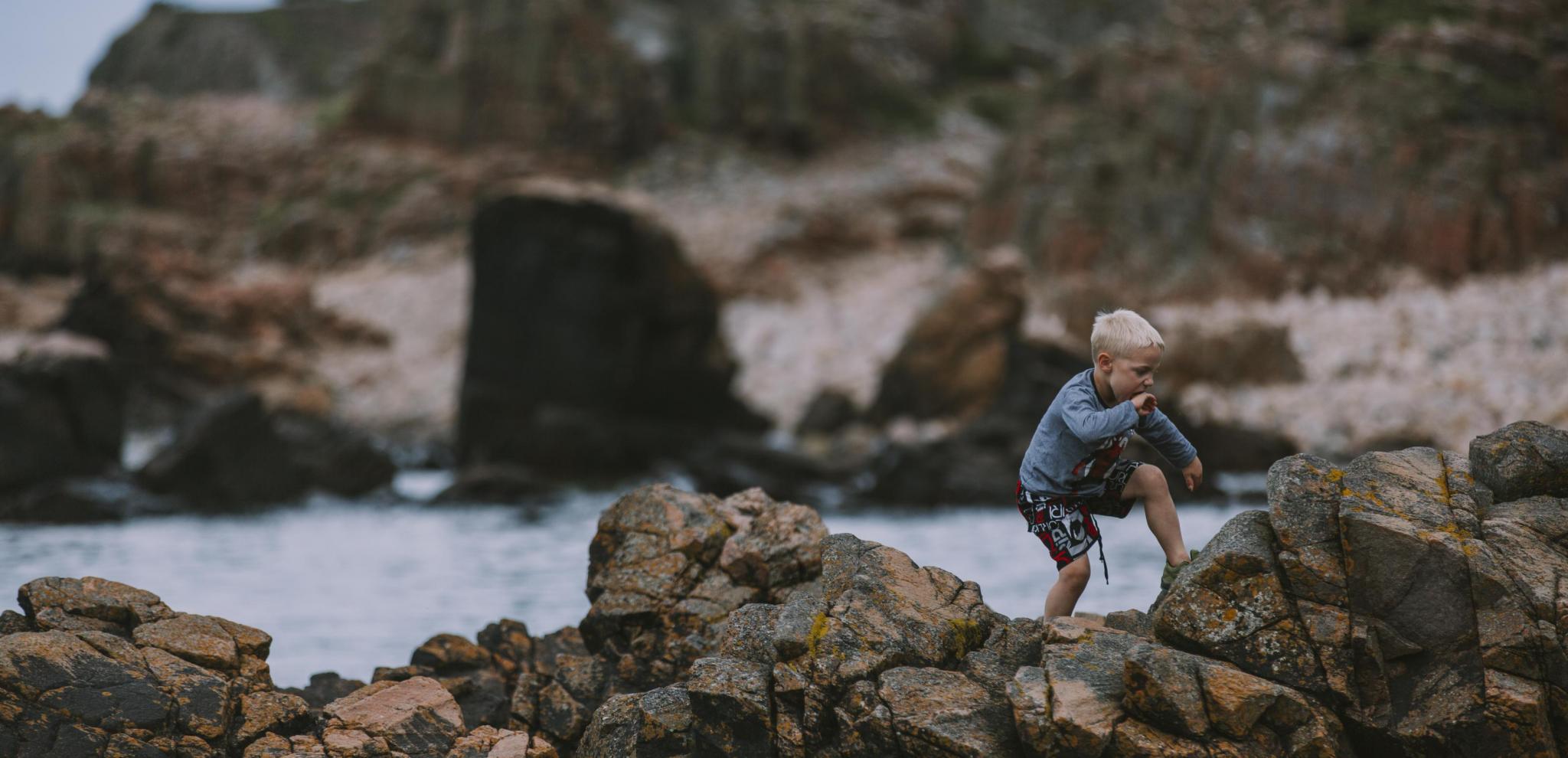 Ein kleiner Junge klettert im Küstengebiet Hovs Hallar über felsige Klippen.