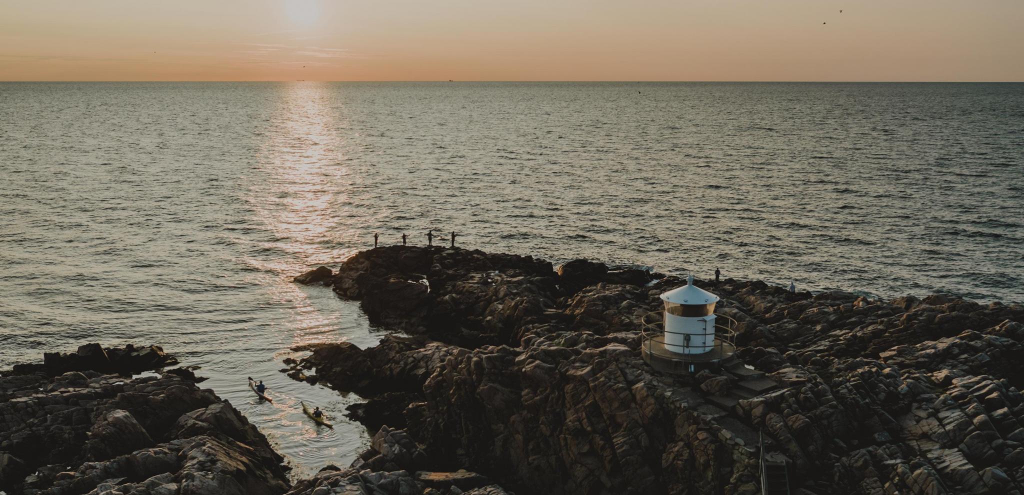 Ein kleiner weißer Leuchtturm am Fuße des Kullabergs im Sonnenuntergang.
