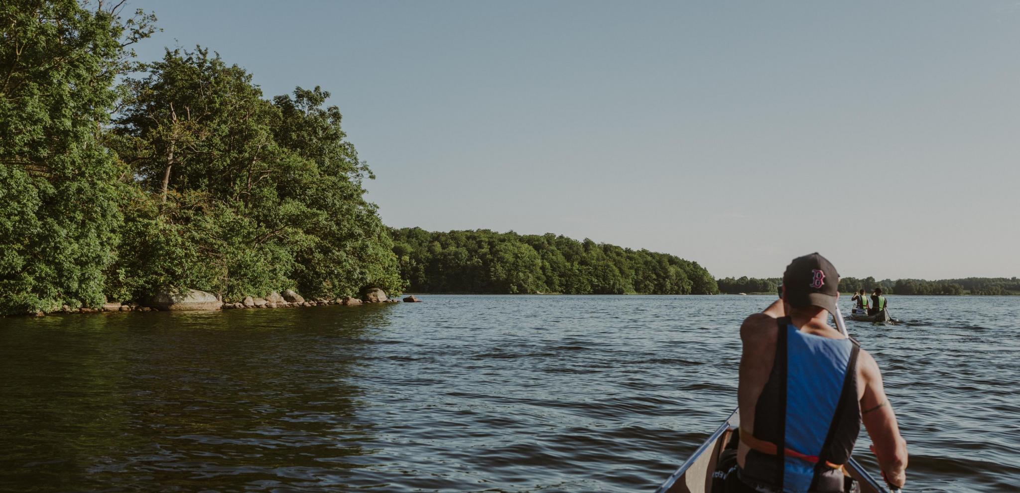 A man paddles a canoe on lake Ivösjö next to a forest