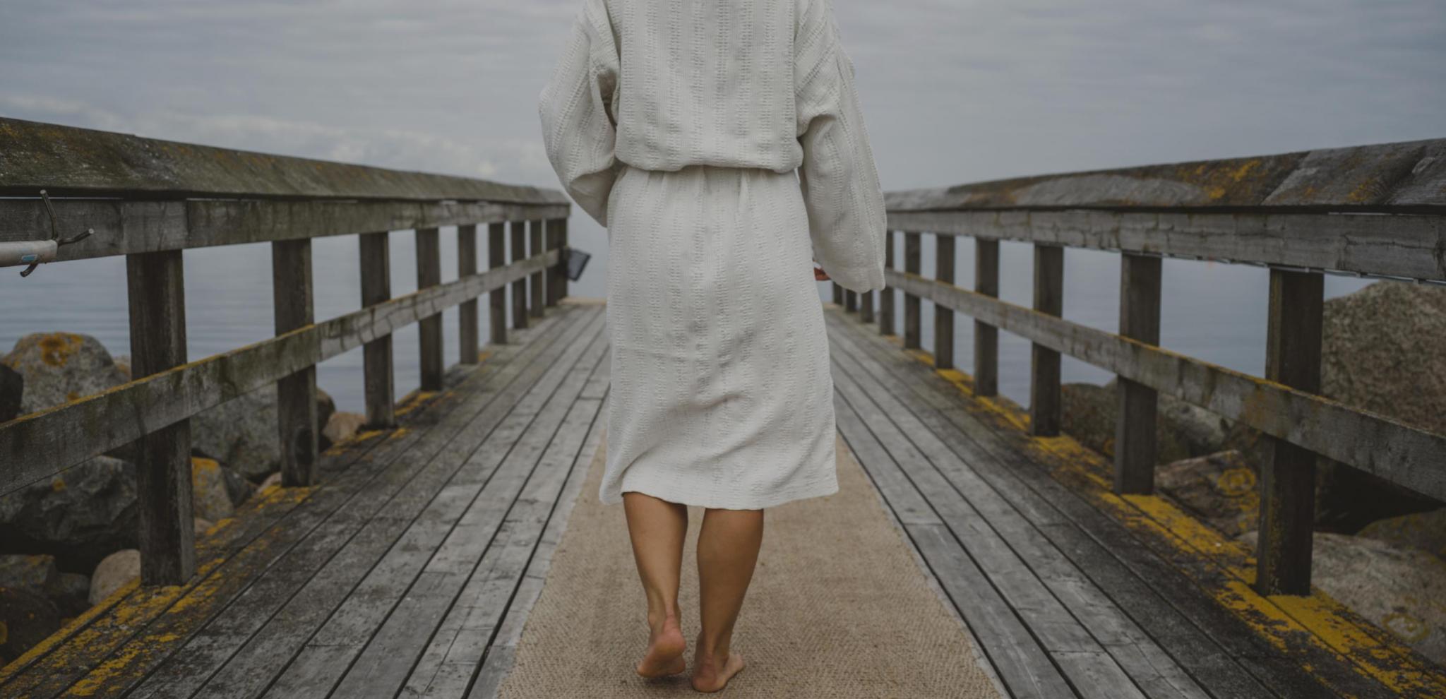 Woman in bathrobe walking on pier to take a swim