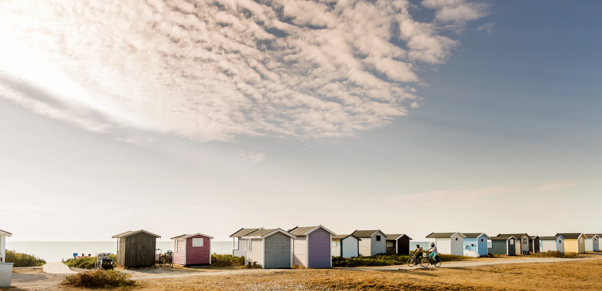 Two cyclists and bathing huts on the sand in Skanör beach on a sunny day