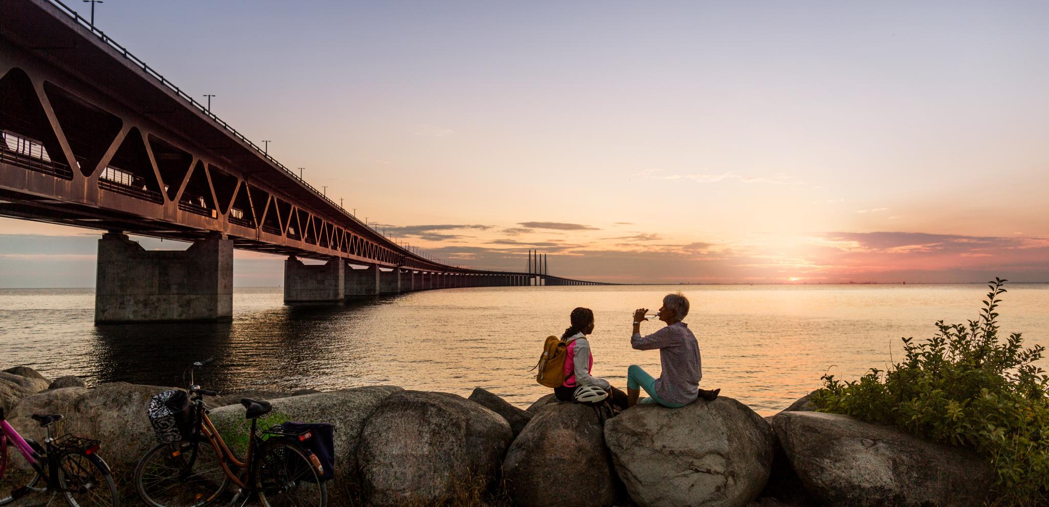 Two people taking a break at sunset next to Öresunds bridge overlooking the sea
