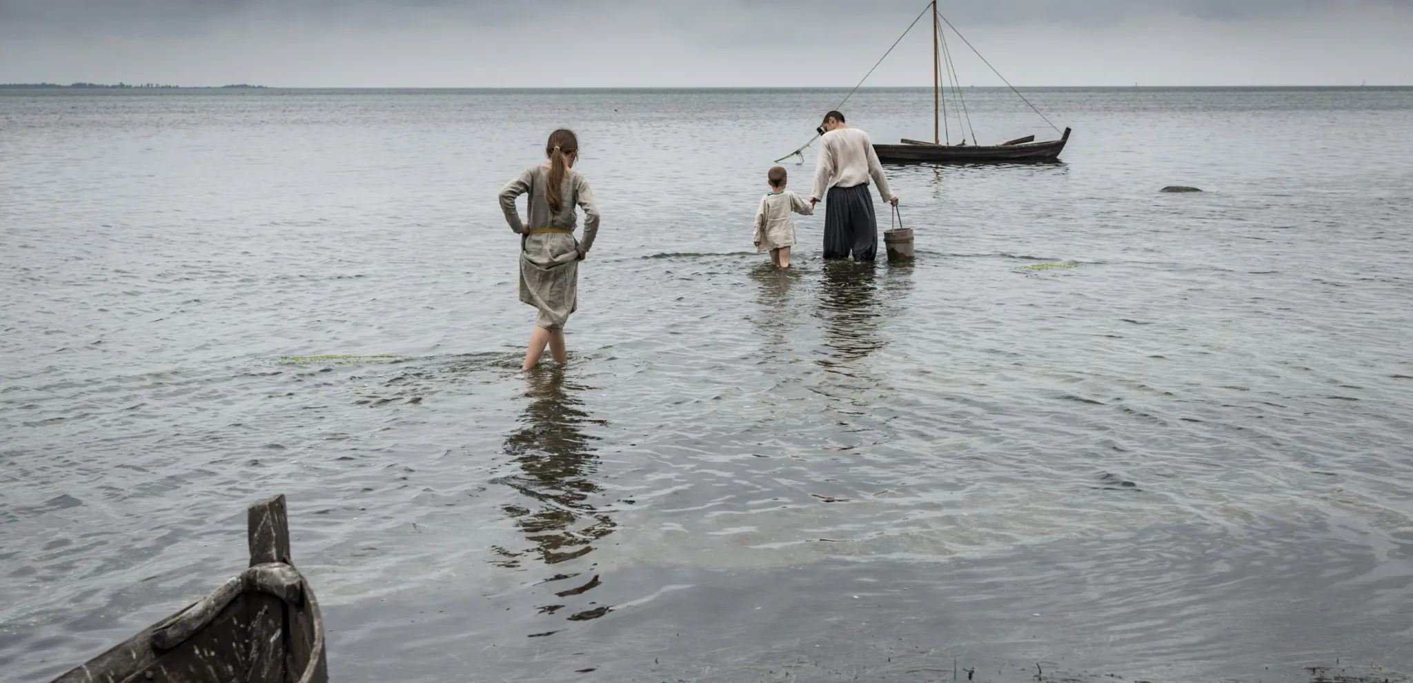 En Vikingafamilj badar i havet intill träbåt