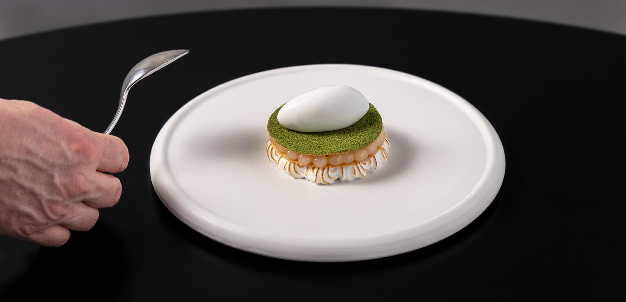 Dessert on  white plate hand holding spoon black table 