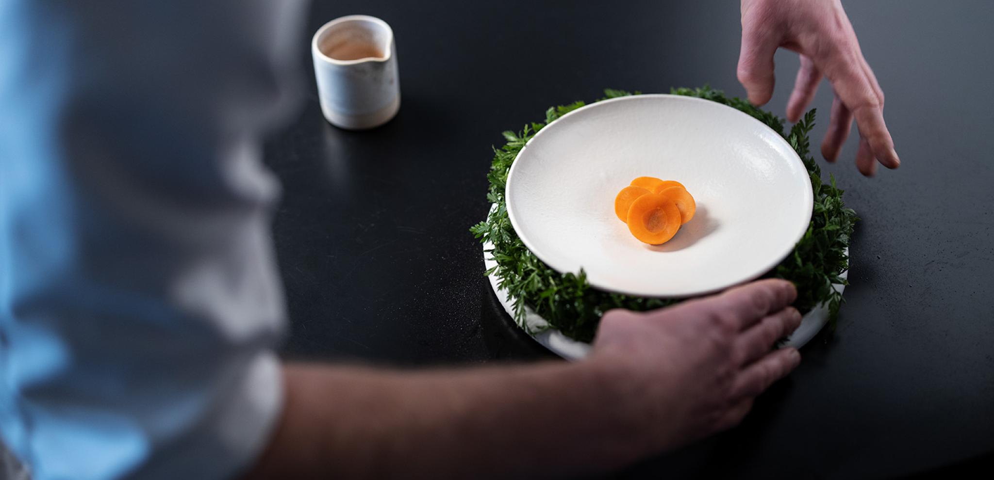 Chef hands around food dish on black table 