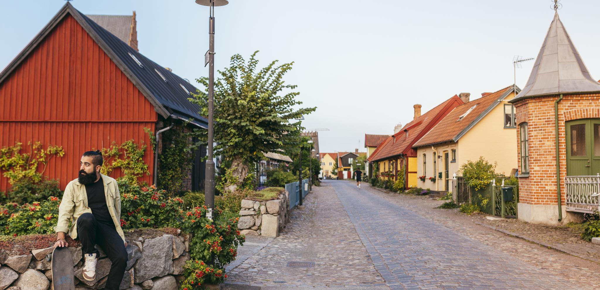 Man with a skateboard is sitting on a wall along a cobbled street in Ahus