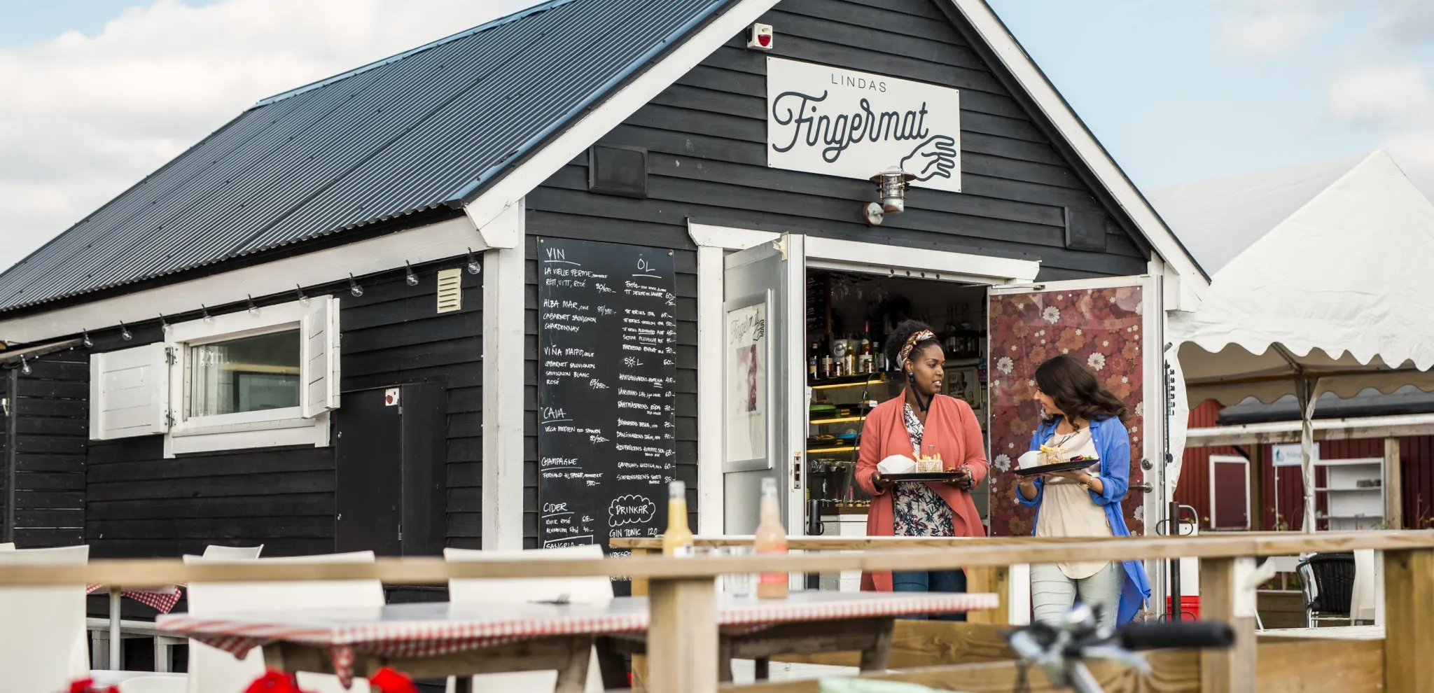 Zwei Frauen kommen mit Essen auf Tabletts aus dem Bistro "Lindas Fingermat".