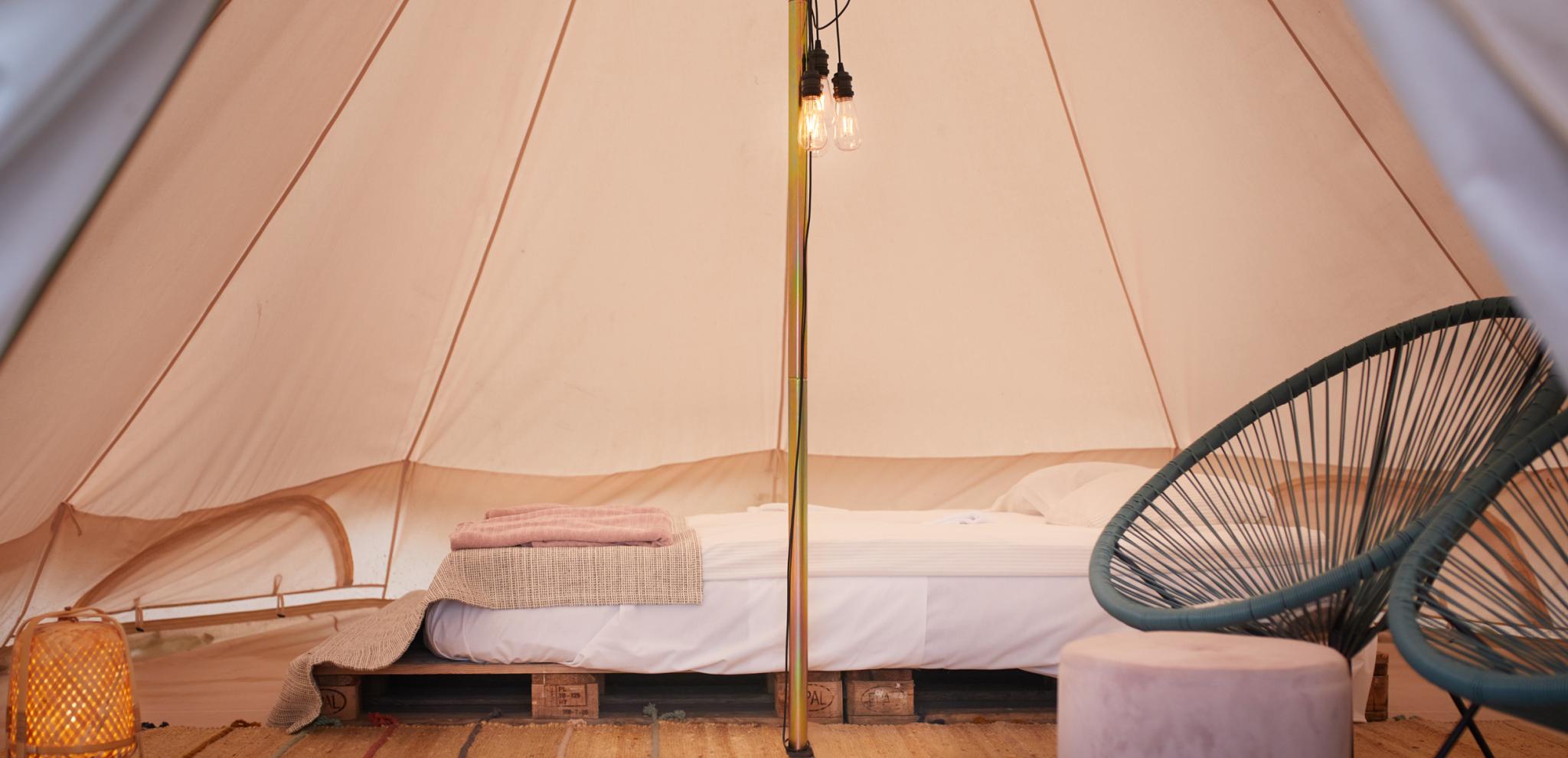 Interior view of glamping tent with wooden flooring, modern black chair, central pole and canvas walls creating cozy accommodation