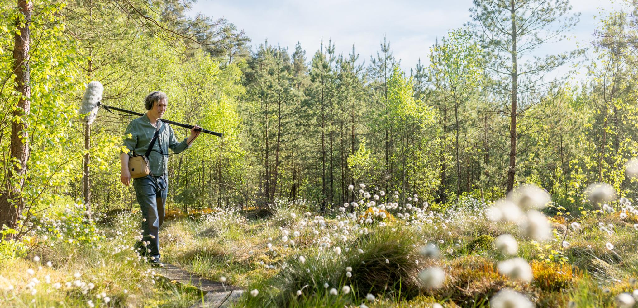 A man with a microphone walking through a forest.