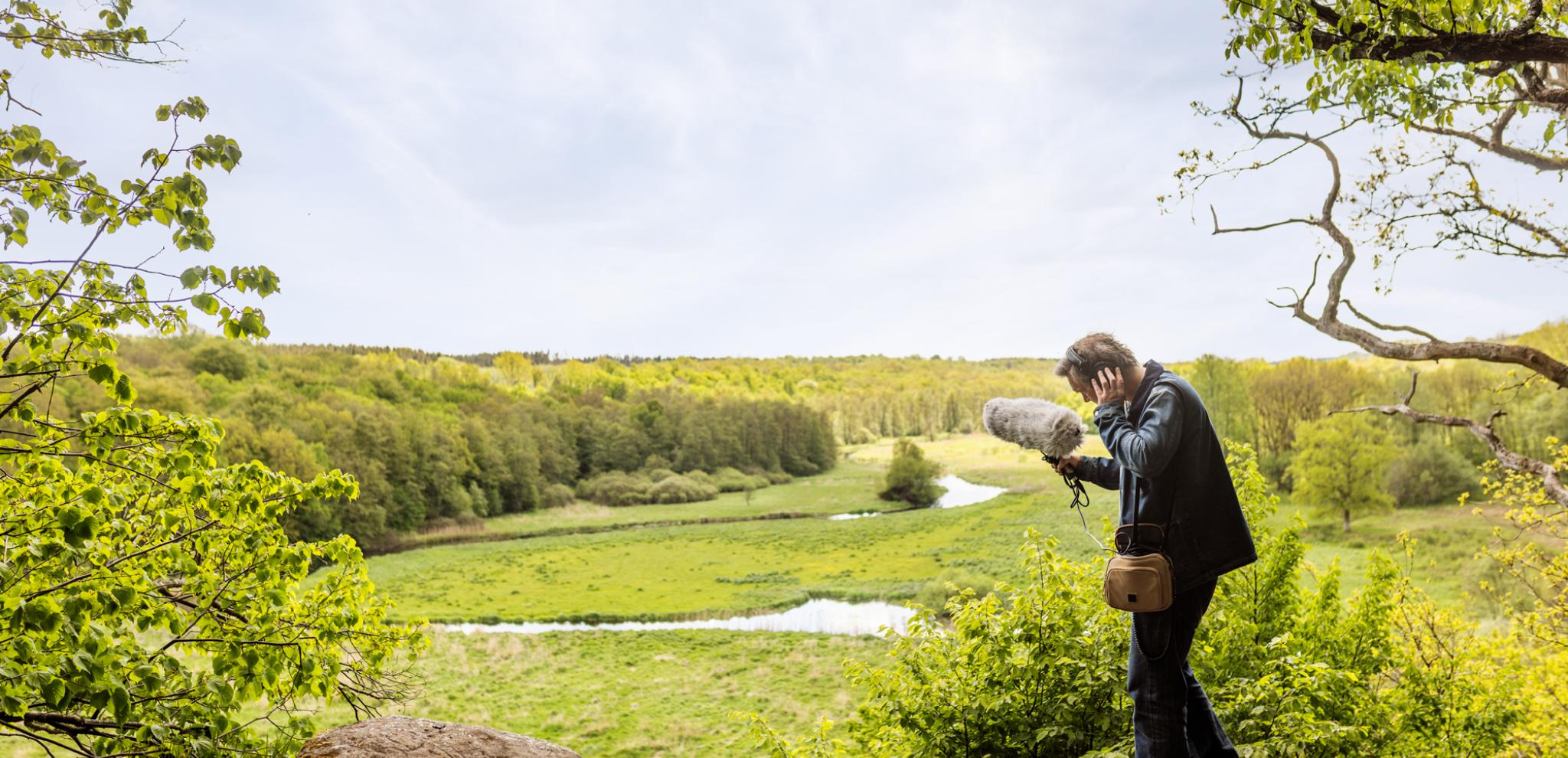 A man standing on top of a rock next to a lush green field and river.