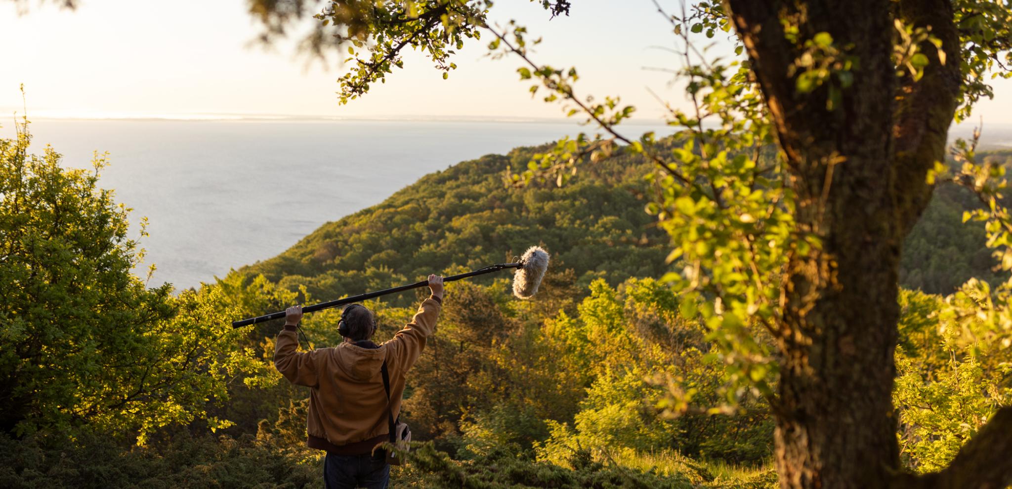 A man walking up a hill carrying a microphone.