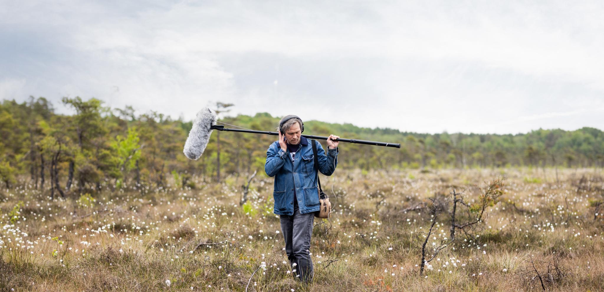 A man in a field holding a microphone.