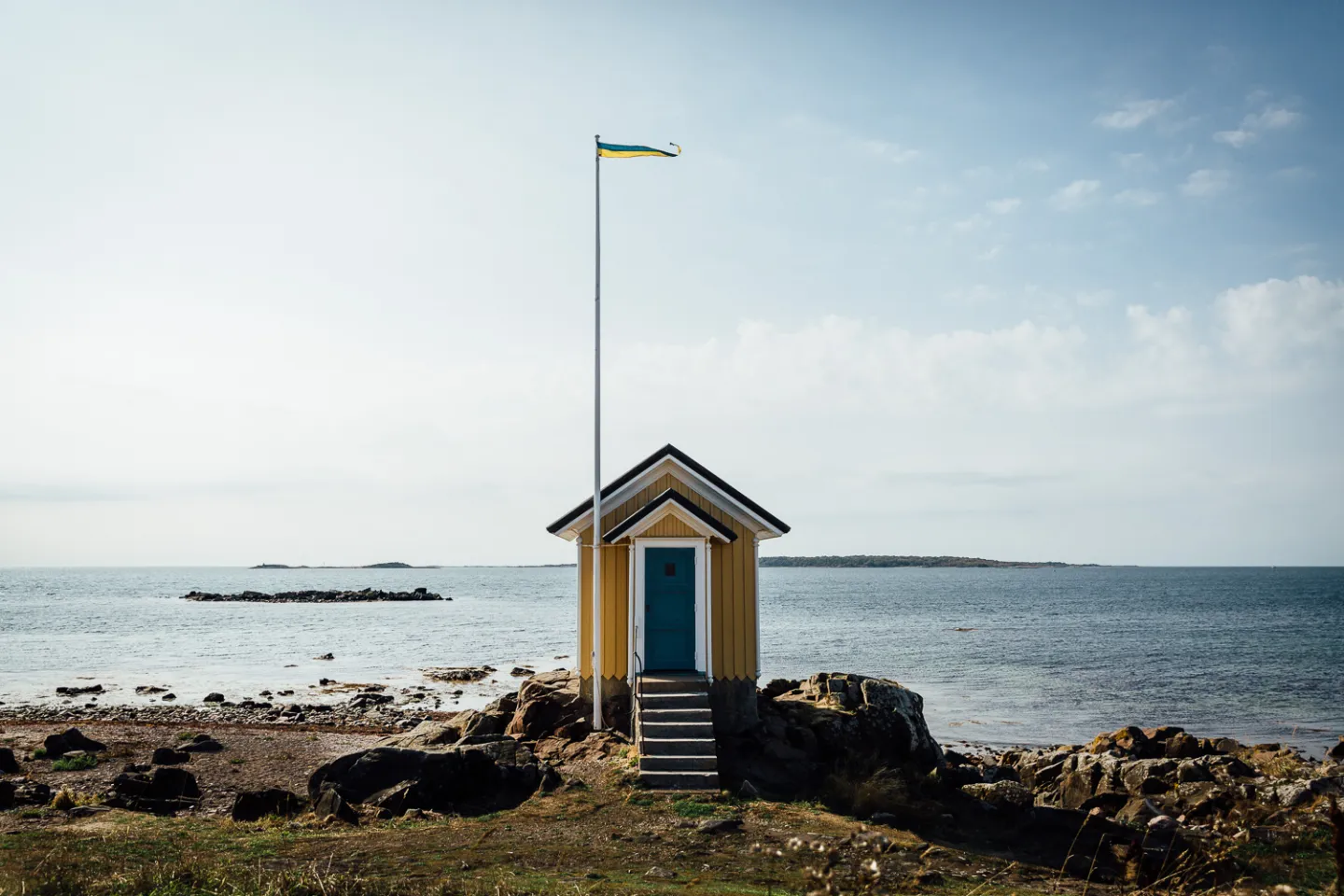 Eine kleine gelbe Hütte an der Küste mit dem Meer im Hintergrund.