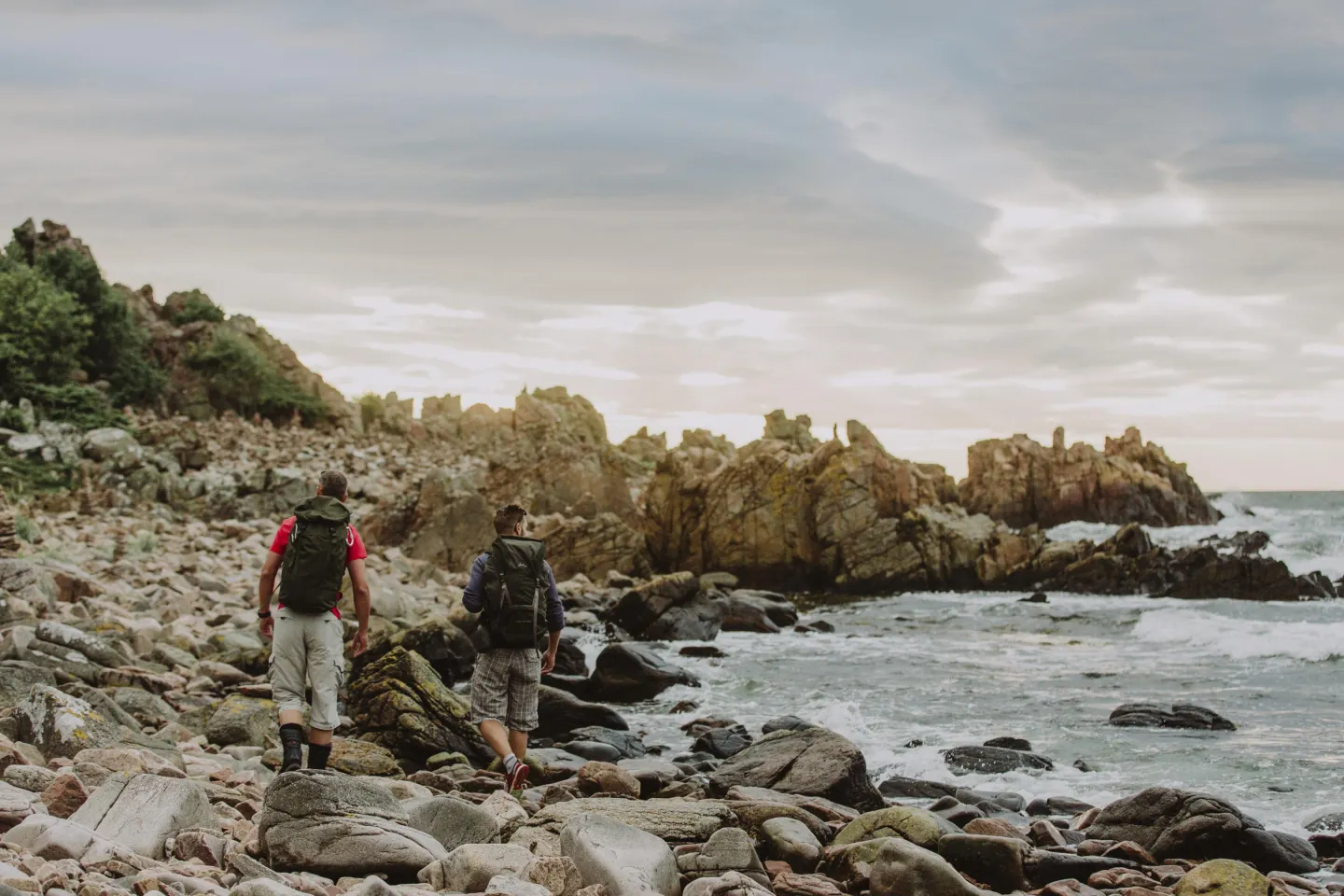 Two men hiking on a beach with large stones at Hovs Hallar