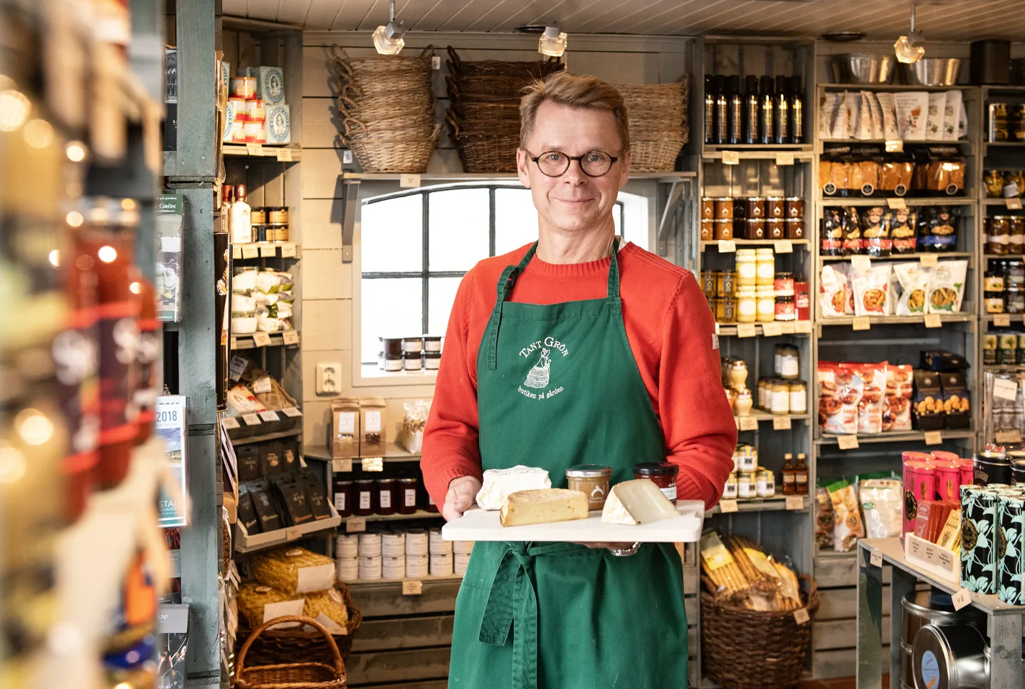 Butikspersonal visar upp en bricka med delikatesser i Tant gröns gårdsbutik