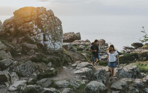 Ein Paar wandert im Naturschutzgebiet Hovs Hallar zwischen Felsen am Meer entlang.