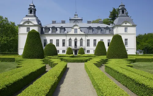 A boxwood garden maze with the fairytale Kronovalls chateaux in the background