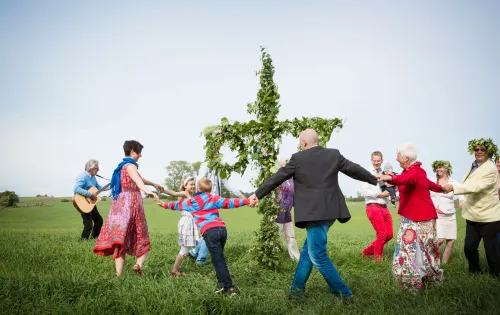 A group of people dancing and singing around the traditional midsummerpole 